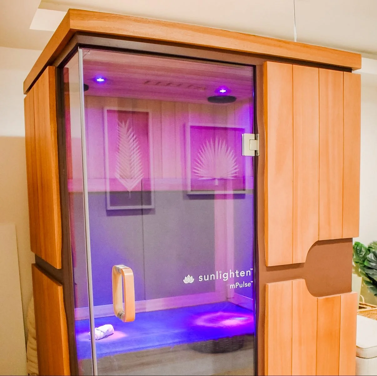A Sunlight mPulse infrared sauna with wooden exterior and glass door reflecting indoor decor, chromotherapy, light therapy