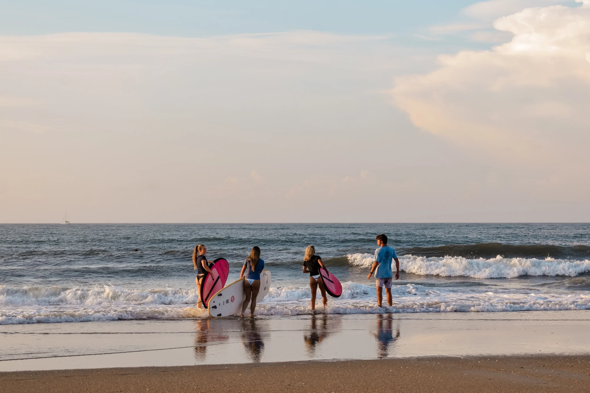 Four young people walking into the ocean with surfboards at the beach during sunset.