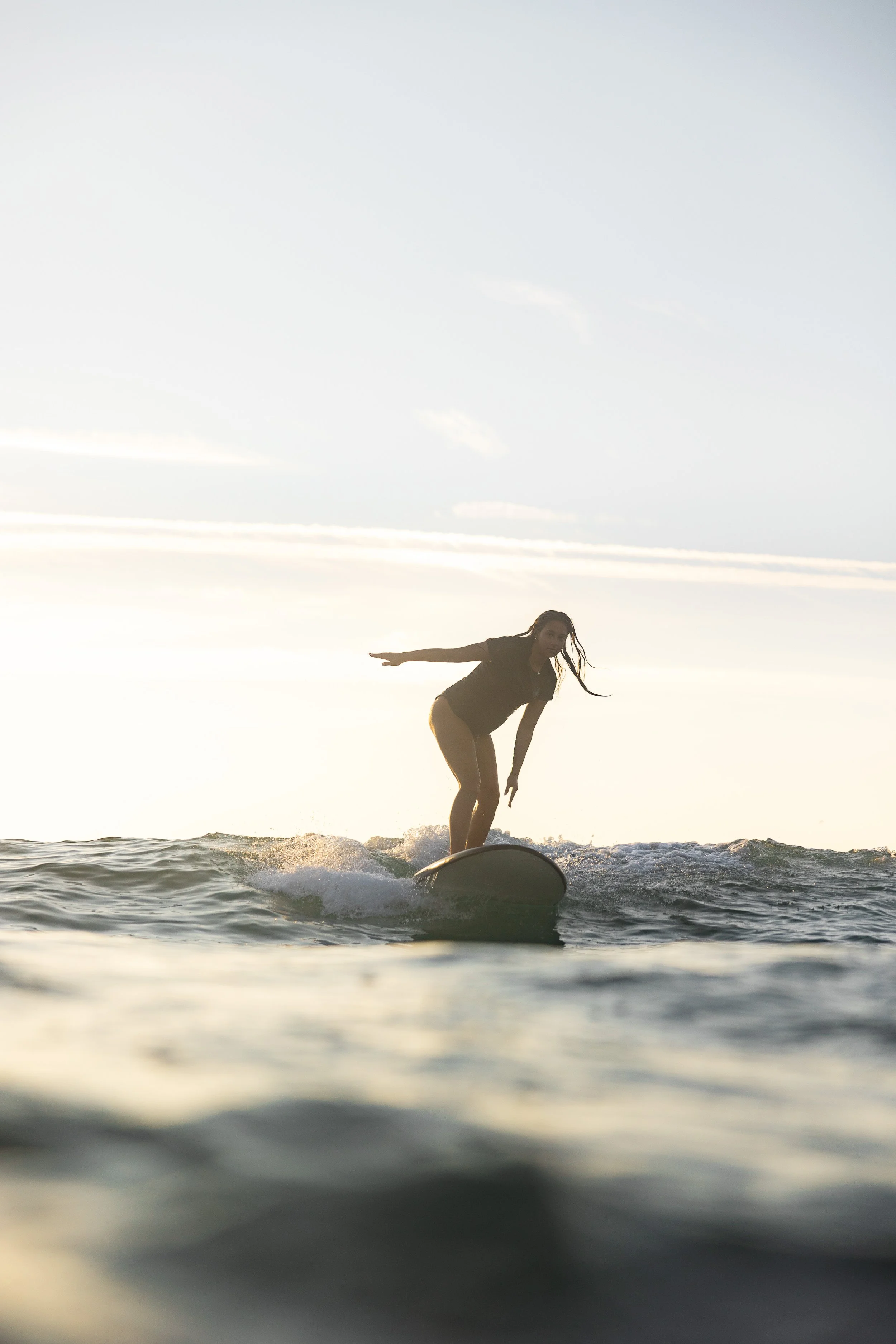 A woman surfing on a surfboard in the ocean during sunset.