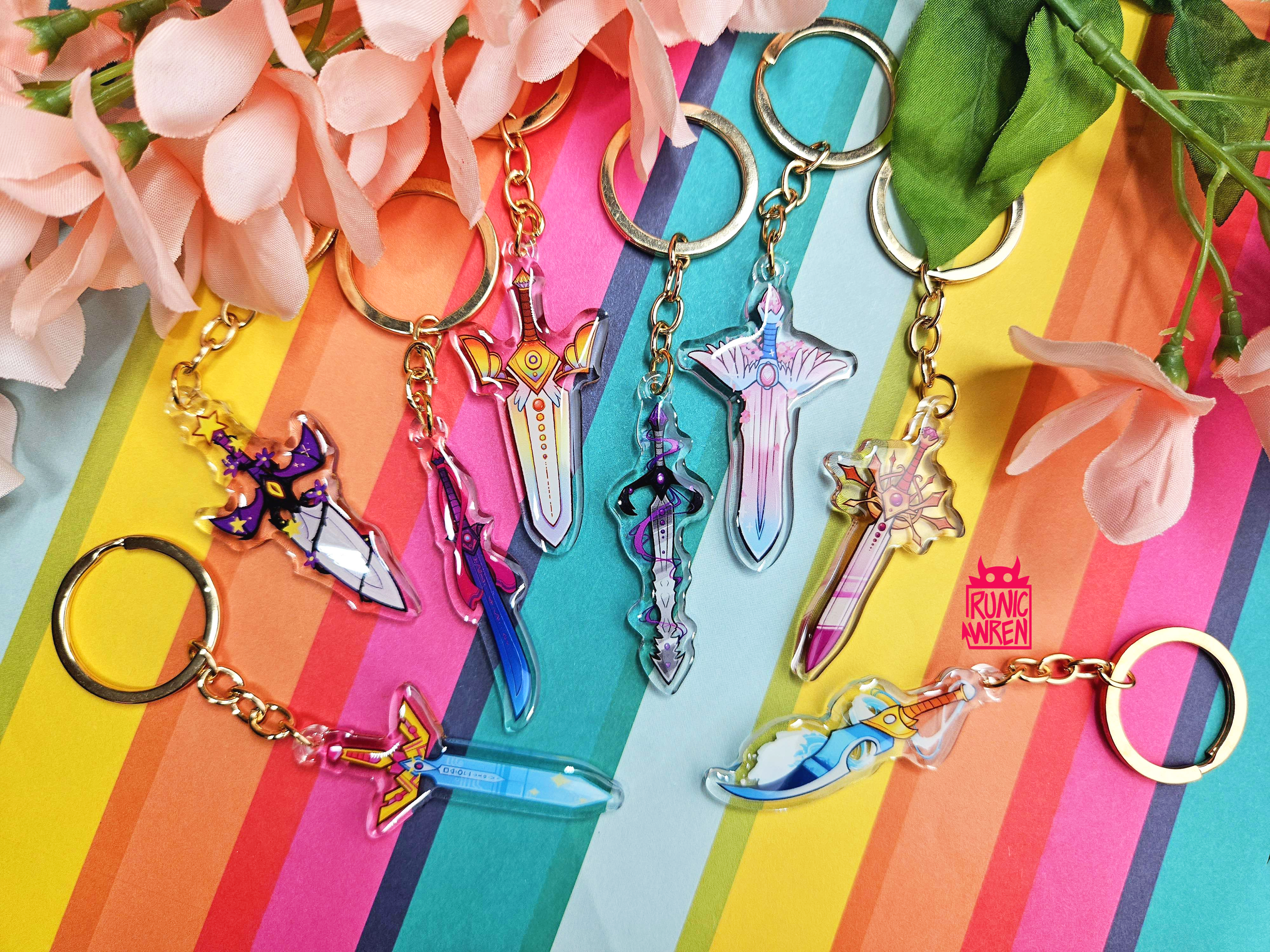 7 Sword keychains lined up on a rainbow background. Each sword is themed after a different pride flag