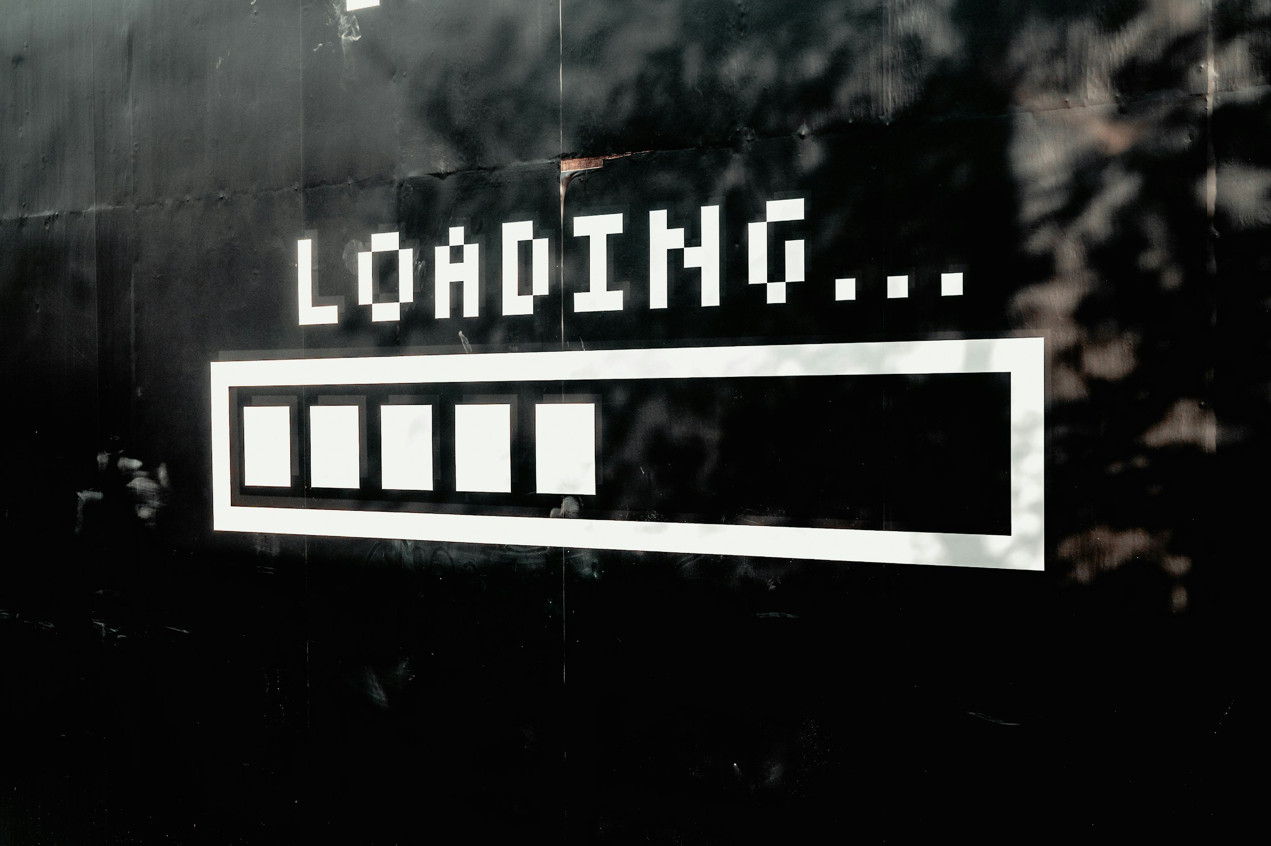 A black wall with a white pixelated sign that reads 'LOADING...' and some white rectangular shapes below it.