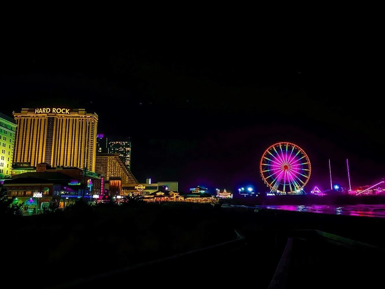 Night view of the Atlantic City New Jersey with illuminated hotels, a brightly lit Ferris wheel, and various neon signs.