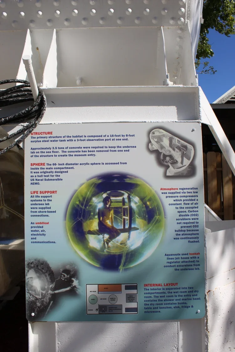 A detailed informational sign about a deep-sea habitat and equipment used for underwater exploration, including sections on the structure, sphere, life support, atmosphere regeneration, internal layout, and images of a diver and underwater scenes.