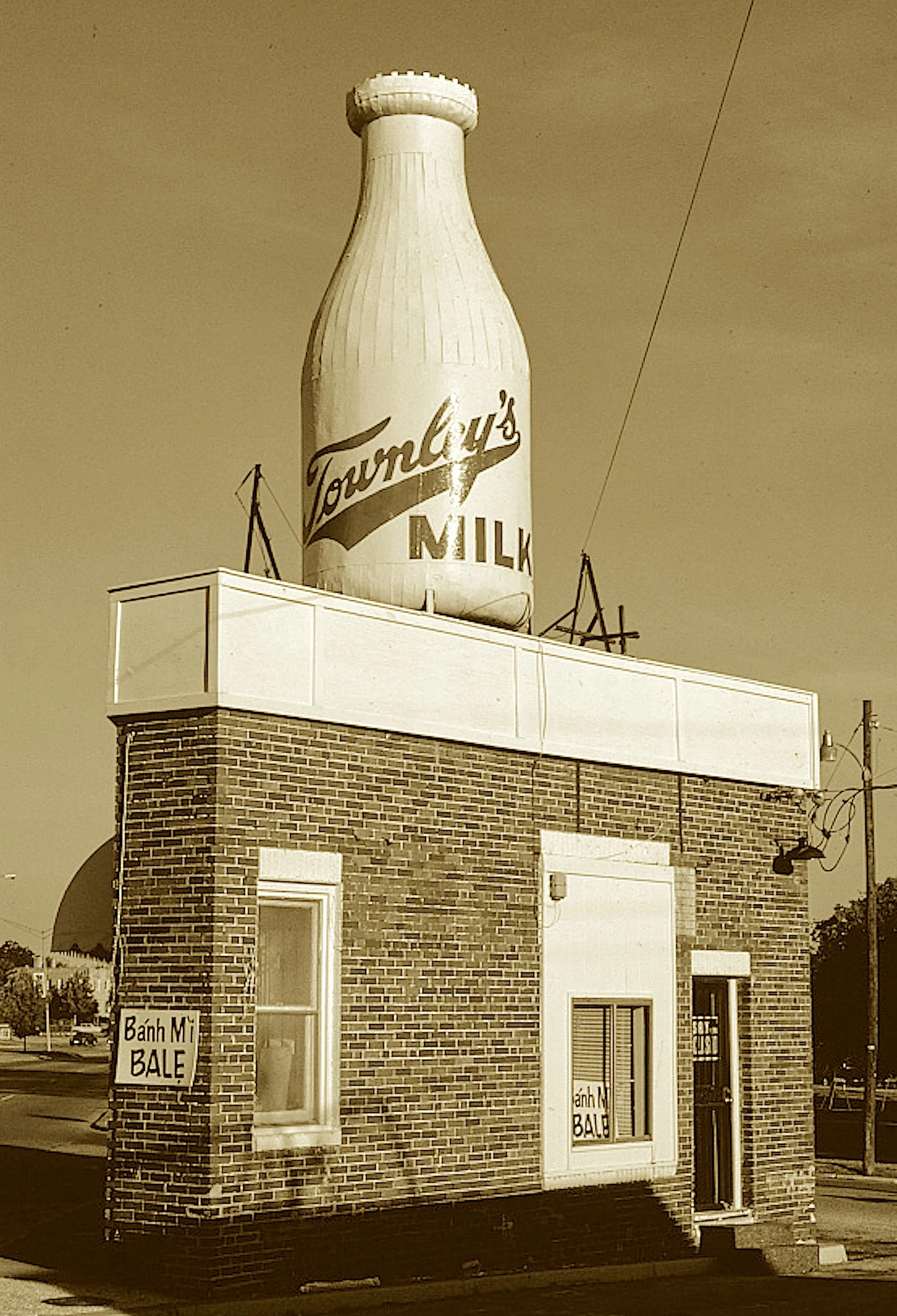 A bottle on top of a building so tight,
It stood in the fork of a three-way bite.
From trolley stop corner to dairyland claim,
Its milk bottle roof brought mimetic fame.
Though tiny in size, it's tall in renown—
A Route 66 legend in bottle-topped cro