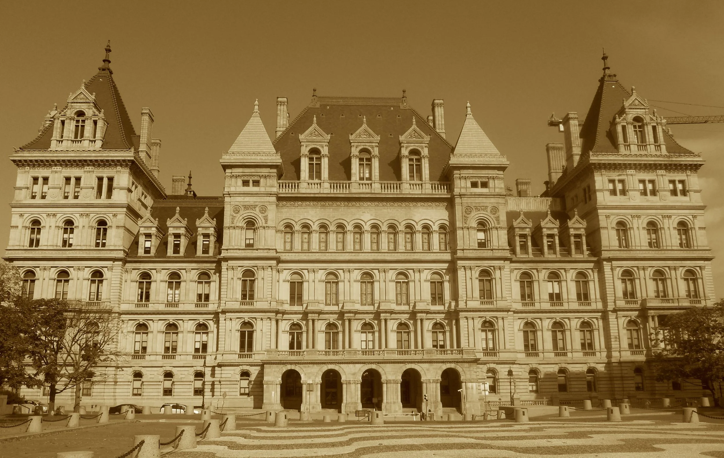 No dome on this throne of executive power,
But grand granite walls and a million-dollar tower.
With stairs that ascend in Richardson’s style,
Through corridors echoing marble and guile.
This house of laws took decades to shape—
A state in stone with