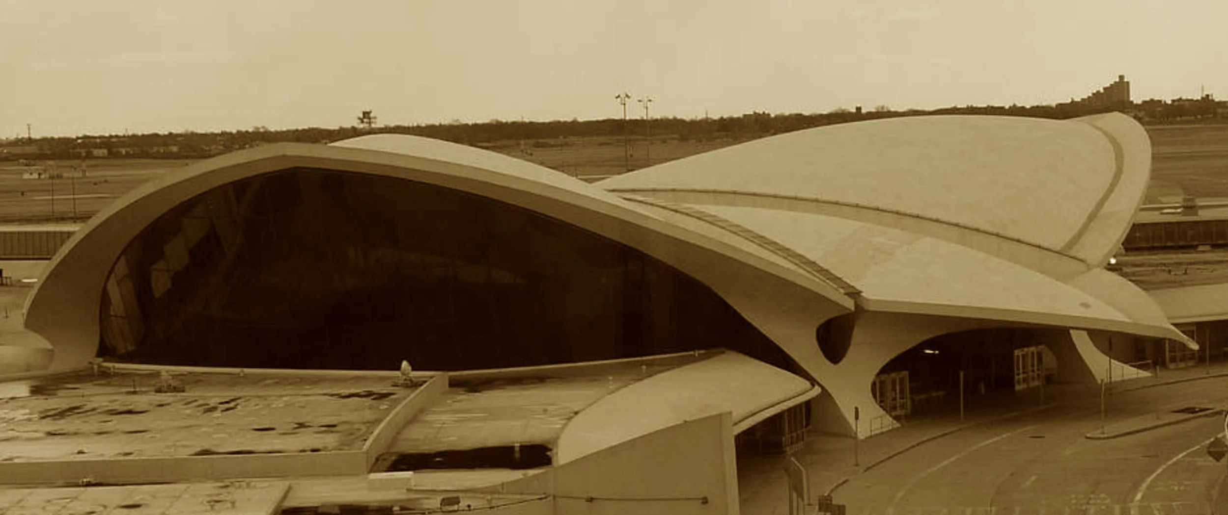 With concrete wings and soaring flair,
It froze mid-century in the air.
Eero Saarinen cast the scene,
Where travel once felt sleek and clean.
Now not for planes but dreams anew—
A hotel dressed in retro view.