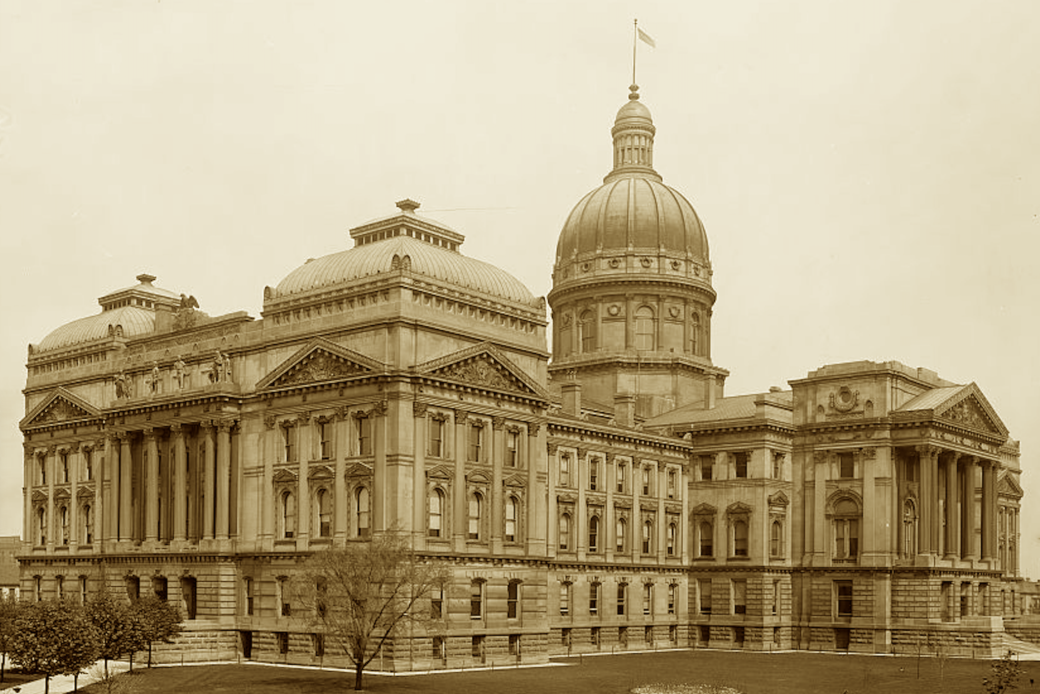 Five capitols stood ‘fore this one took place,
With domes and columns full of grace.
A limestone cross, both wide and grand,
Where May drew plans with Scherrer’s hand.
Now statues on the lawn do stand—
To mark the heart of Hoosier land.