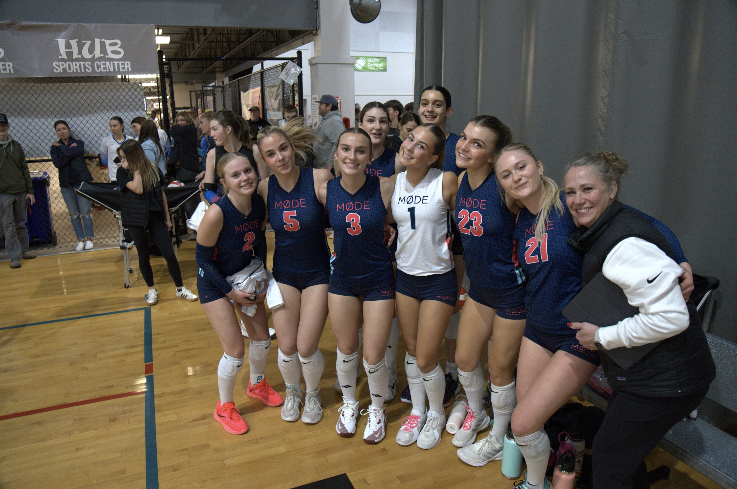 A group of female volleyball players with a coach, posing for a photo in an indoor sports facility.