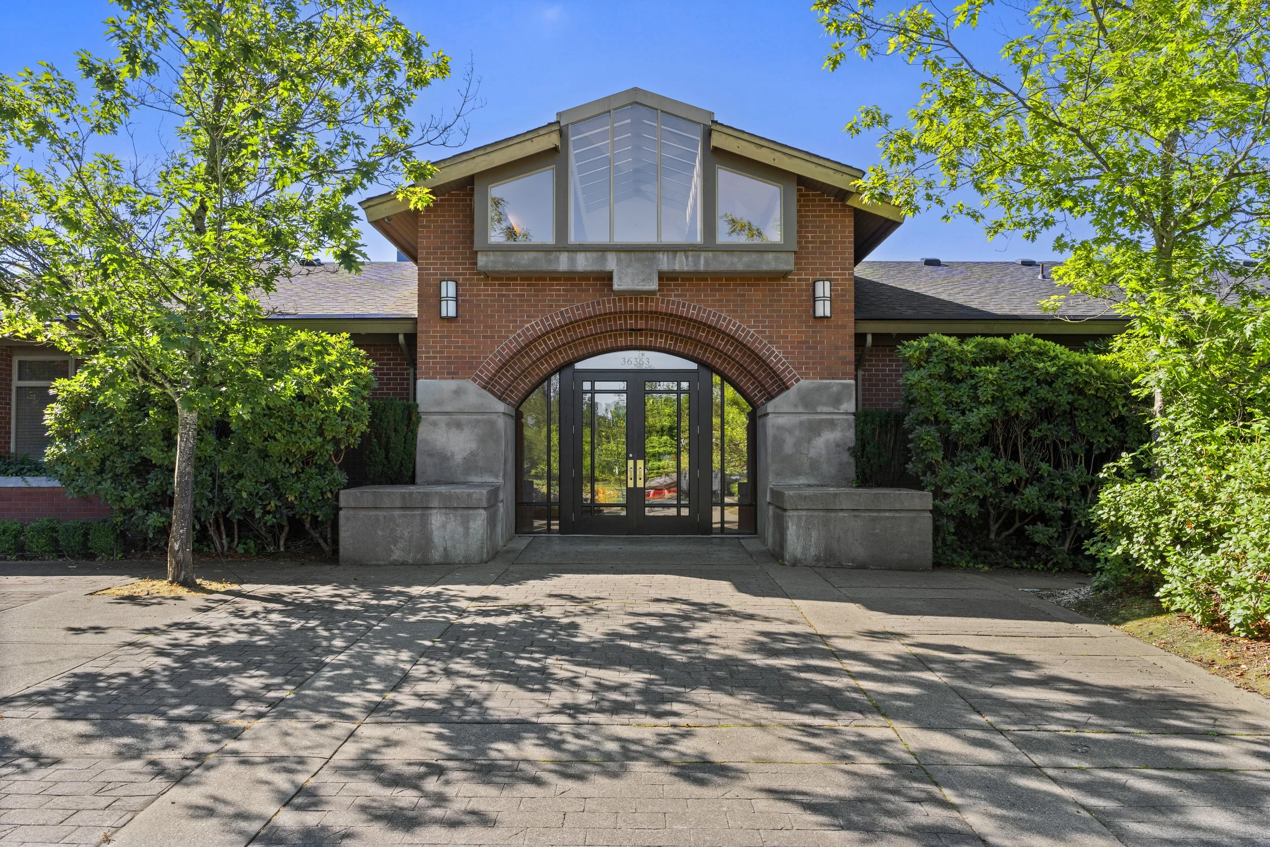 A brick apartment building with a gated entrance, surrounded by trees and bushes, under a clear blue sky.