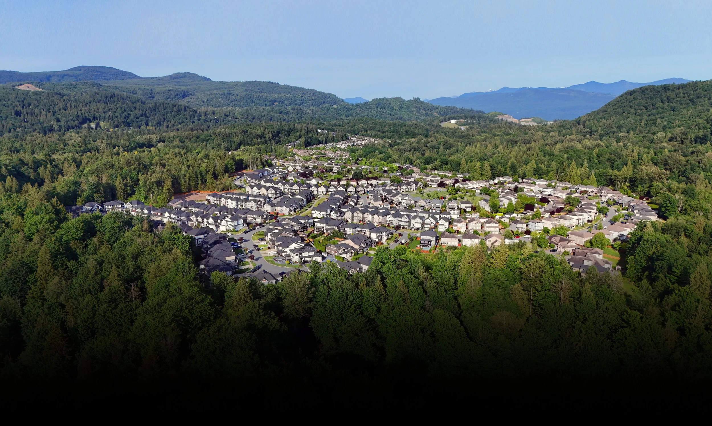 Aerial view of a residential neighborhood surrounded by lush green forests and mountains in the background.