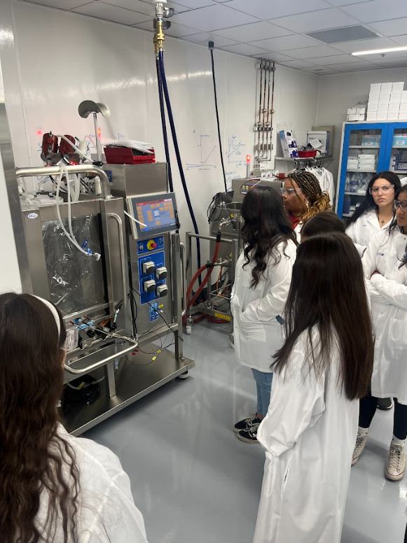 Group of students in lab coats gathered around scientific equipment in a laboratory