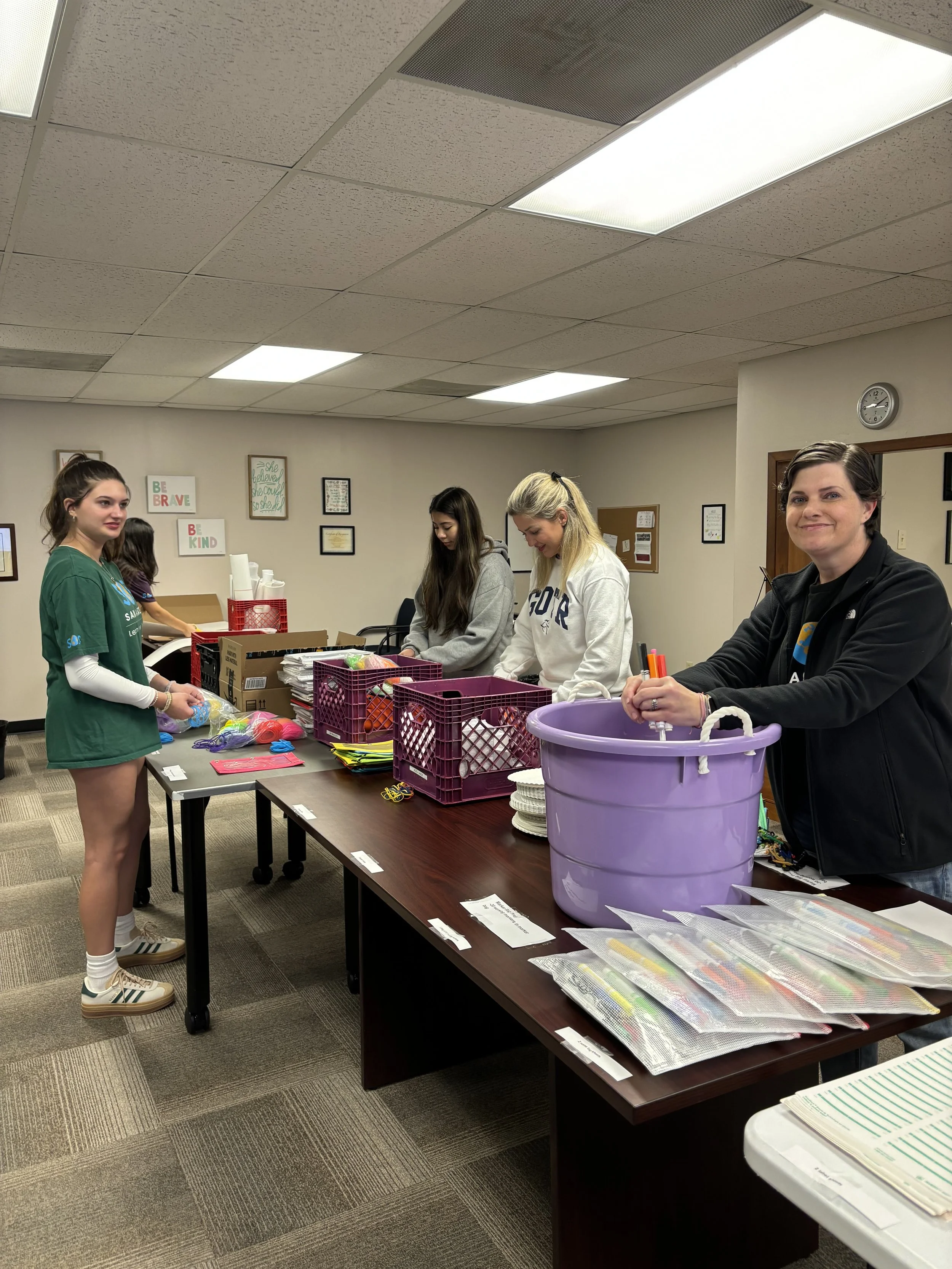 People organizing supplies at a table in a room with educational posters on the walls.