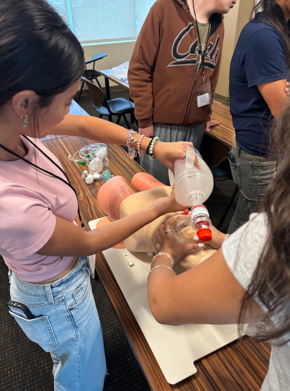 People practicing CPR on a mannequin with a bag valve mask in a classroom setting.