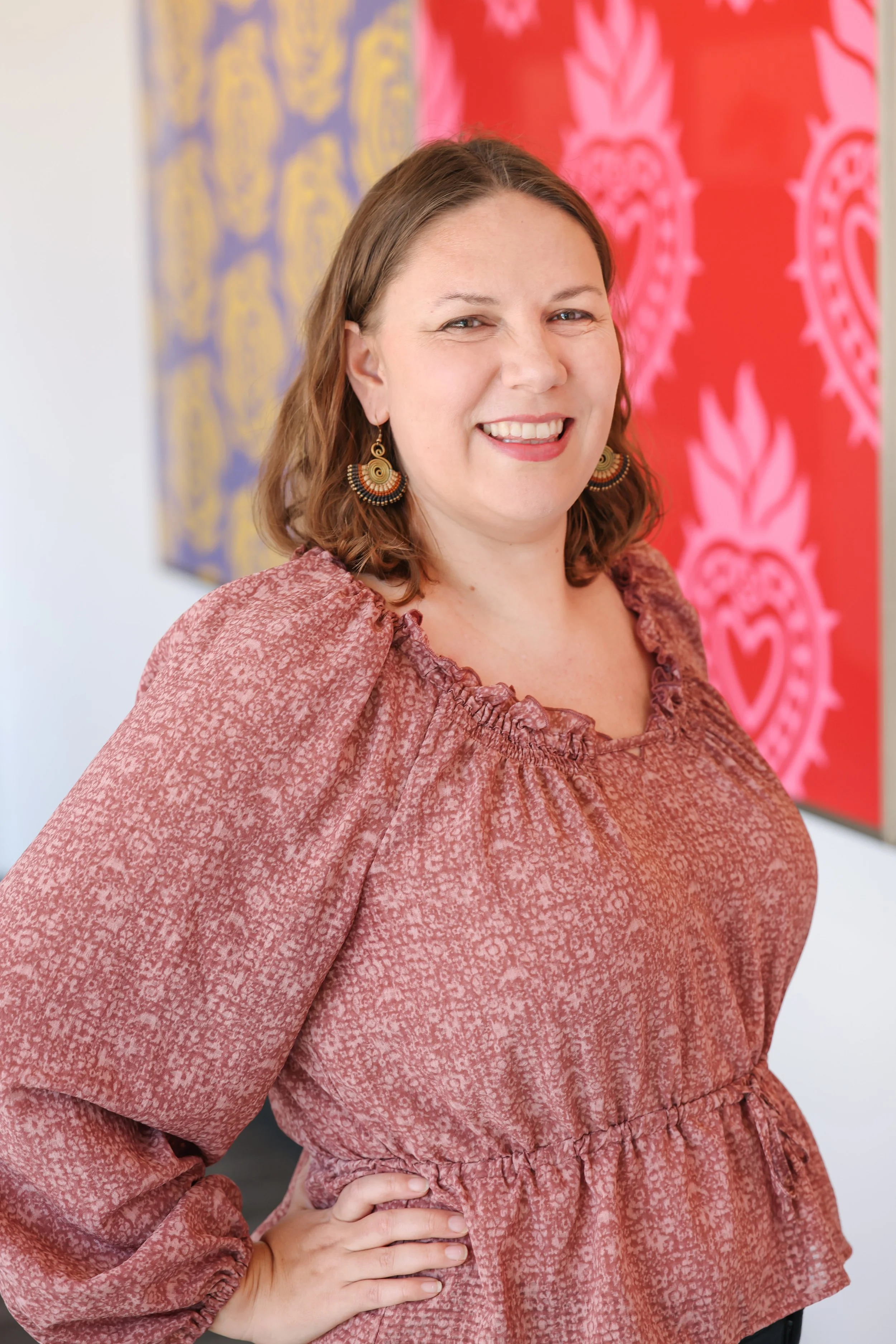A woman smiling with a colorful background of textiles or artwork.