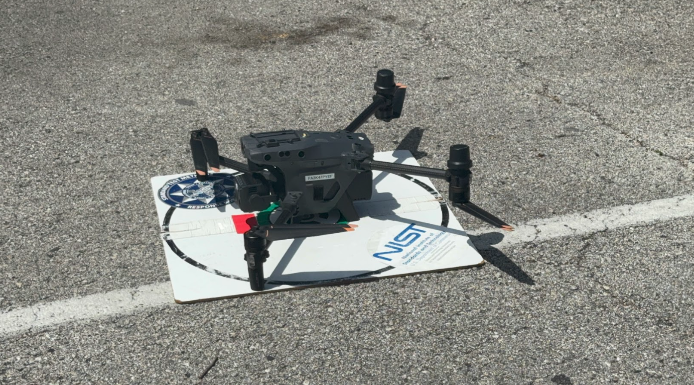 A black drone lying on a white poster board on a paved surface, getting ready to take off.