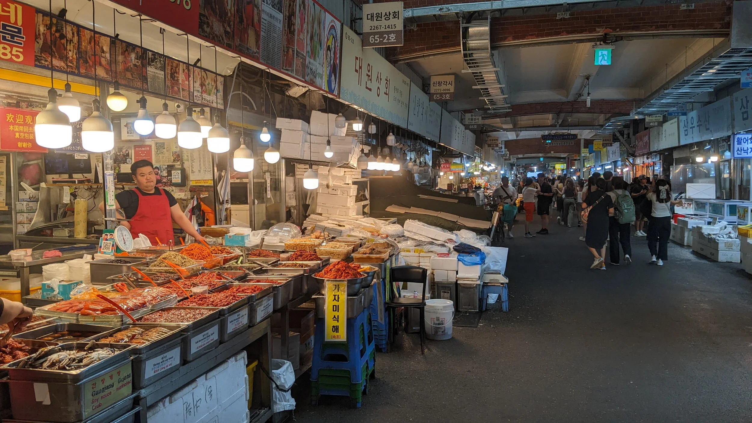 Indoor traditional market with seafood and various food stalls, people shopping and browsing.