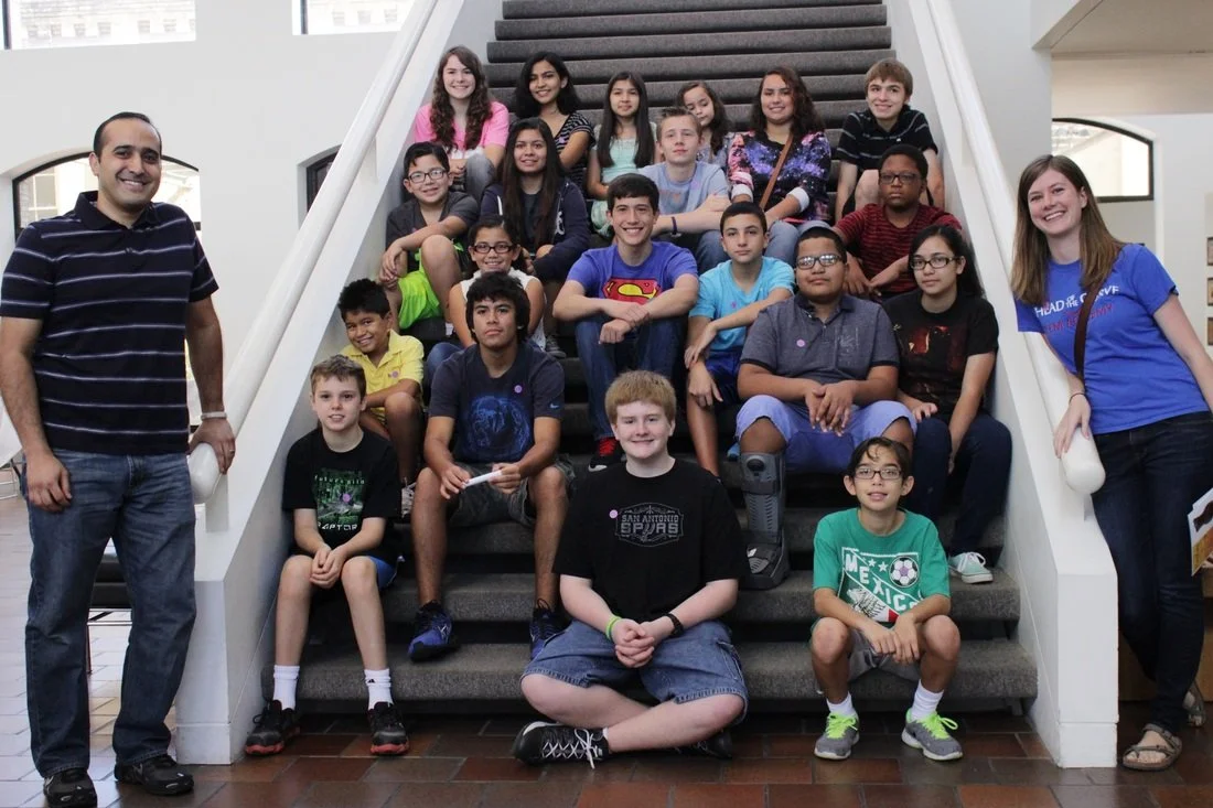 Group of children and two adults on stairs in a building, smiling for the photo.