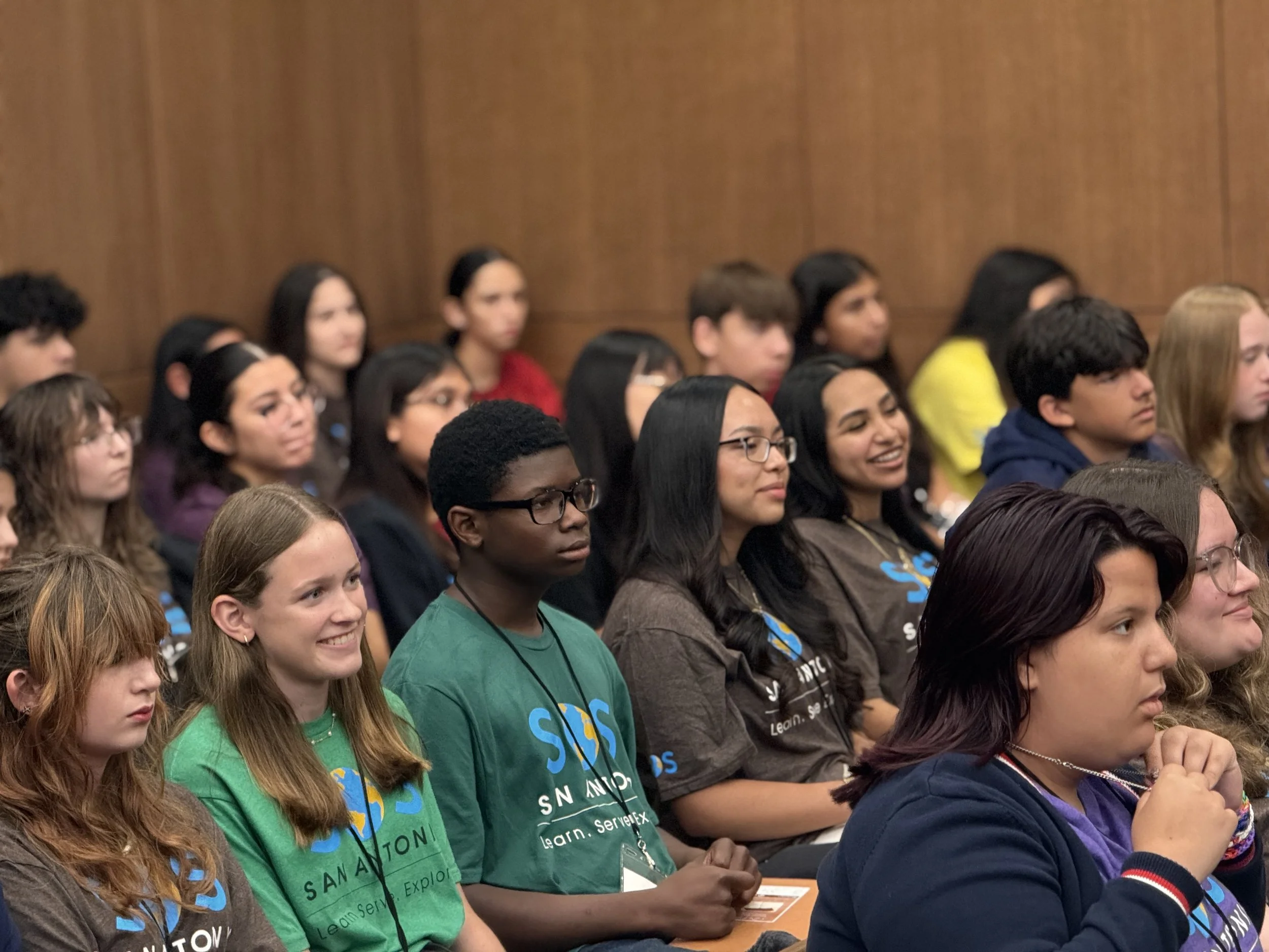 A diverse group of young students attentively listening to a presentation in a courtroom for the Exploring Justice Program (EJP).