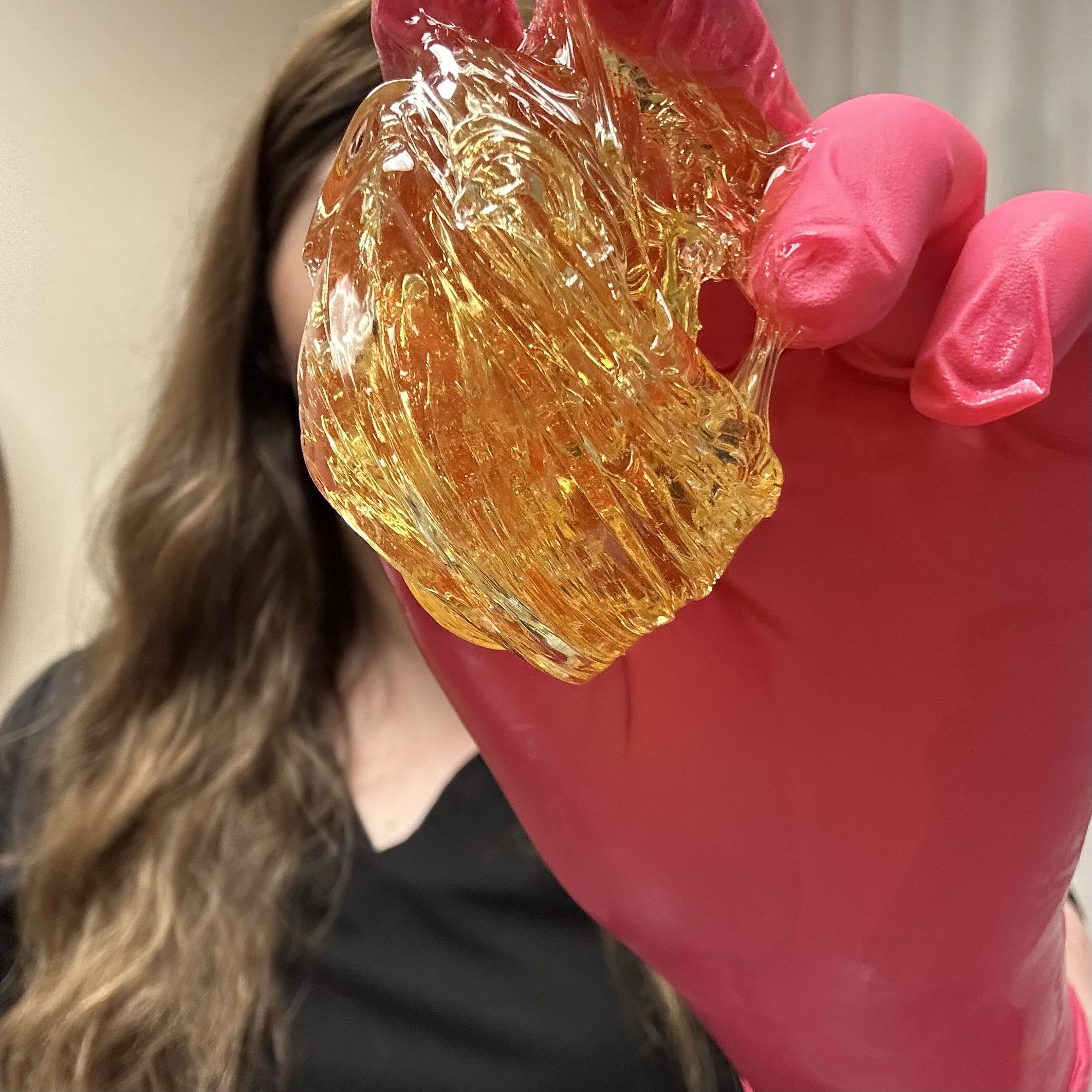 A person wearing a pink glove holding a ball of sugar, used for sugaring hair removal.