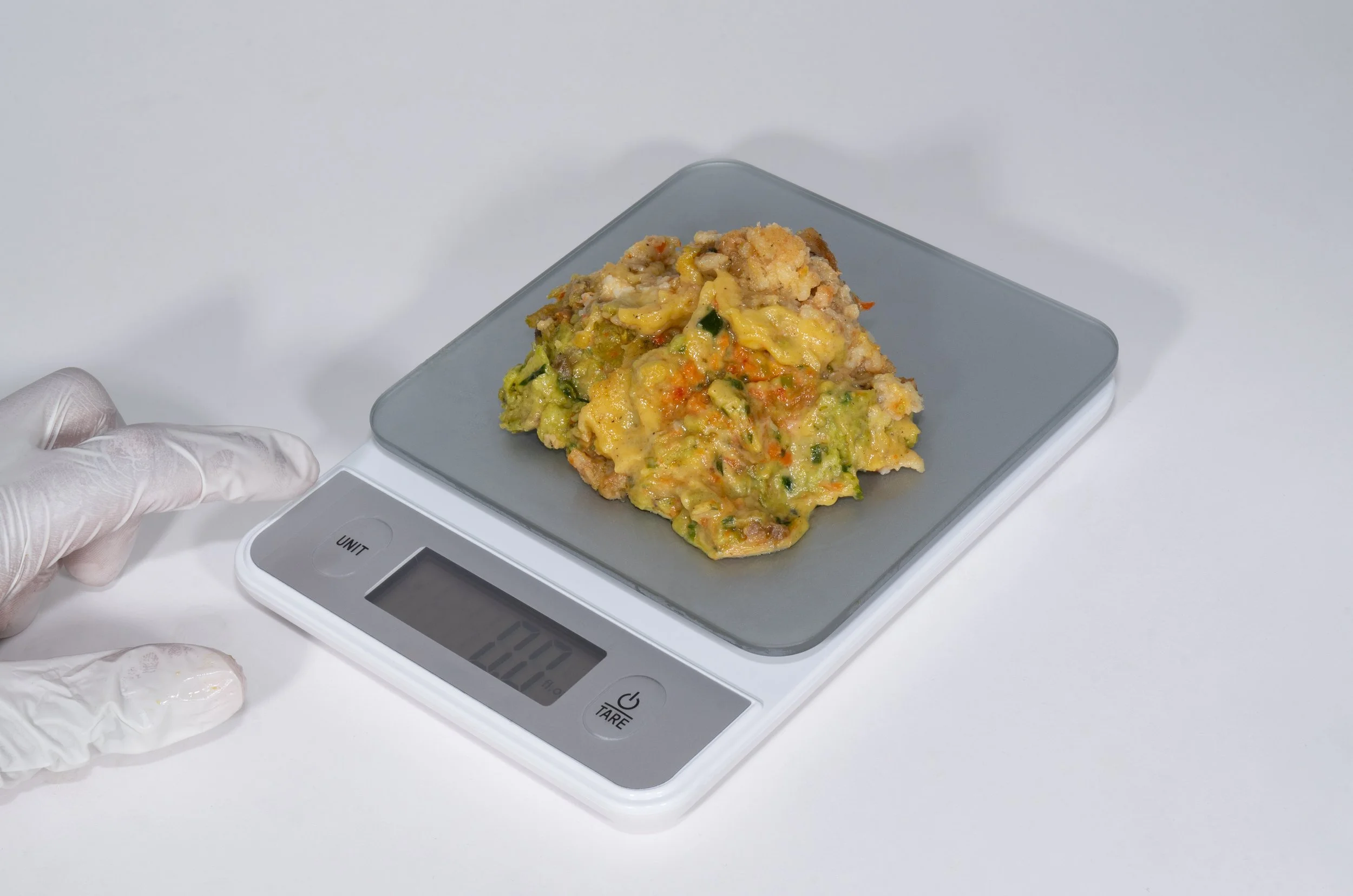 Food sample on digital scale with gloved hand nearby
