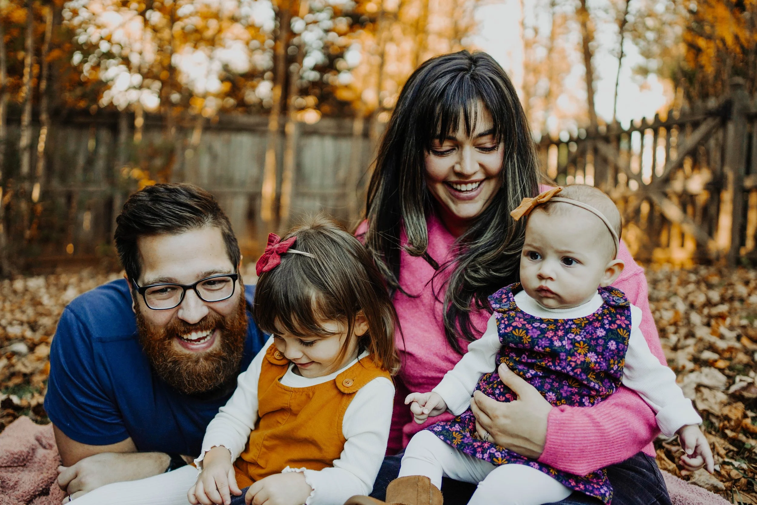 A happy family outdoors in autumn, sitting on the ground covered with fallen leaves, smiling and spending time together.