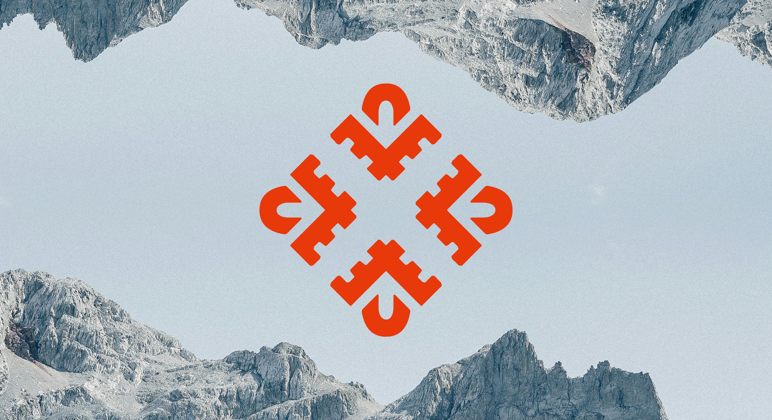 Mountain landscape with rocky peaks and a light blue sky, featuring a red geometric symbol in the center.