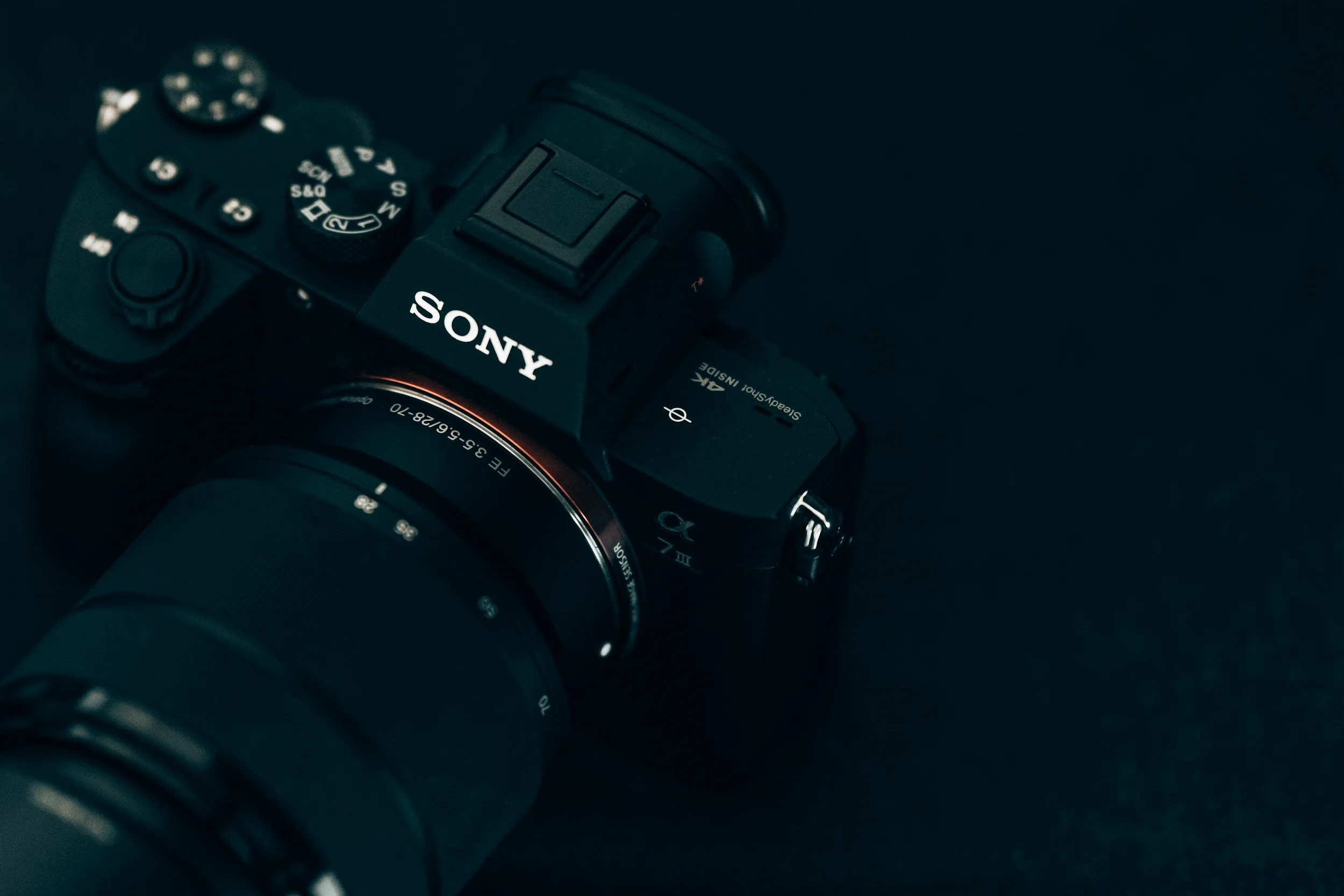 Black Sony camera with a large zoom lens and several buttons, set against a dark background.