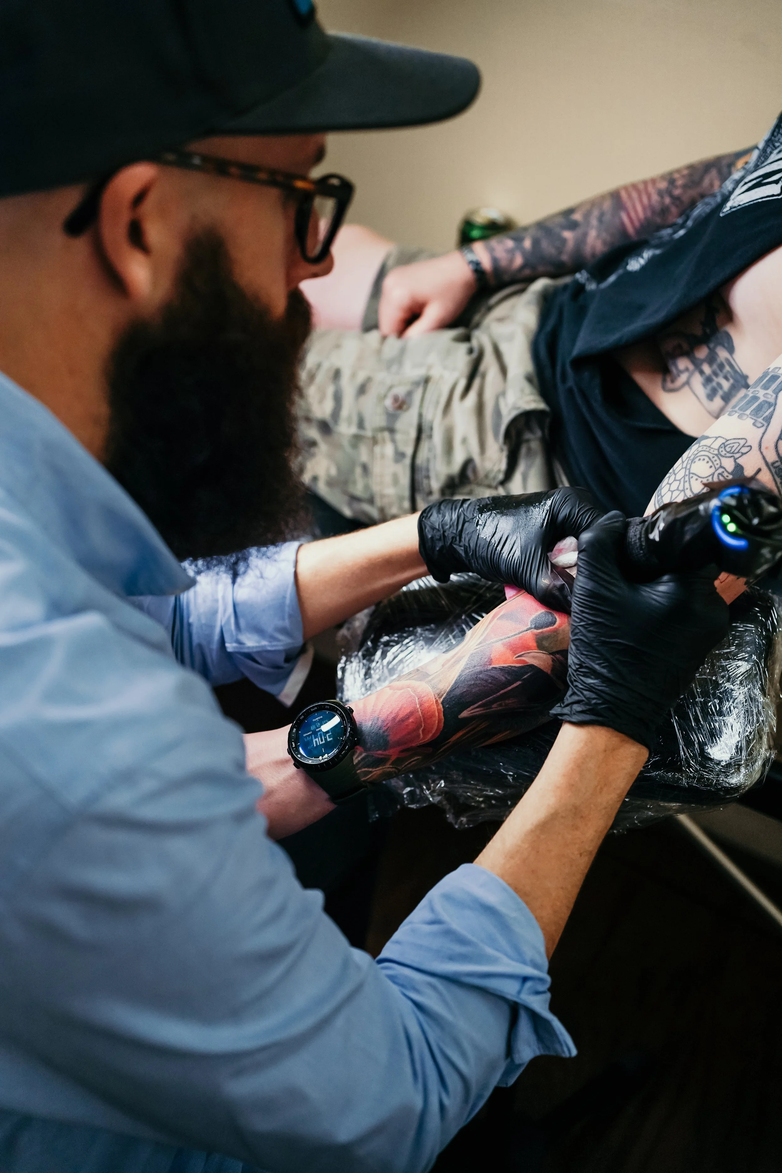 Tattoo artist tattooing a person's arm in a studio setting.