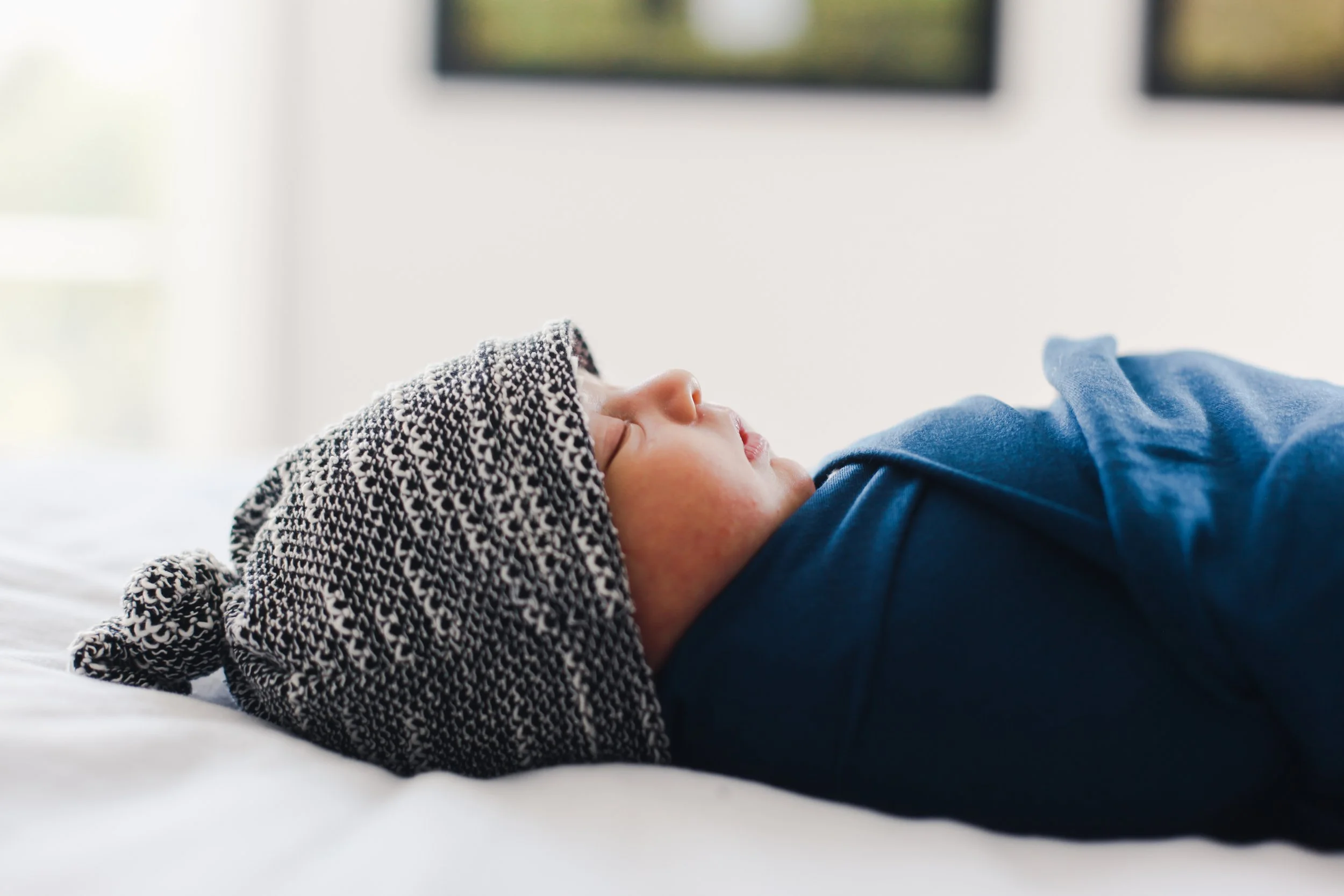 A young child lying on a bed with a black and white patterned knit hat and a blue shirt, sleeping peacefully.