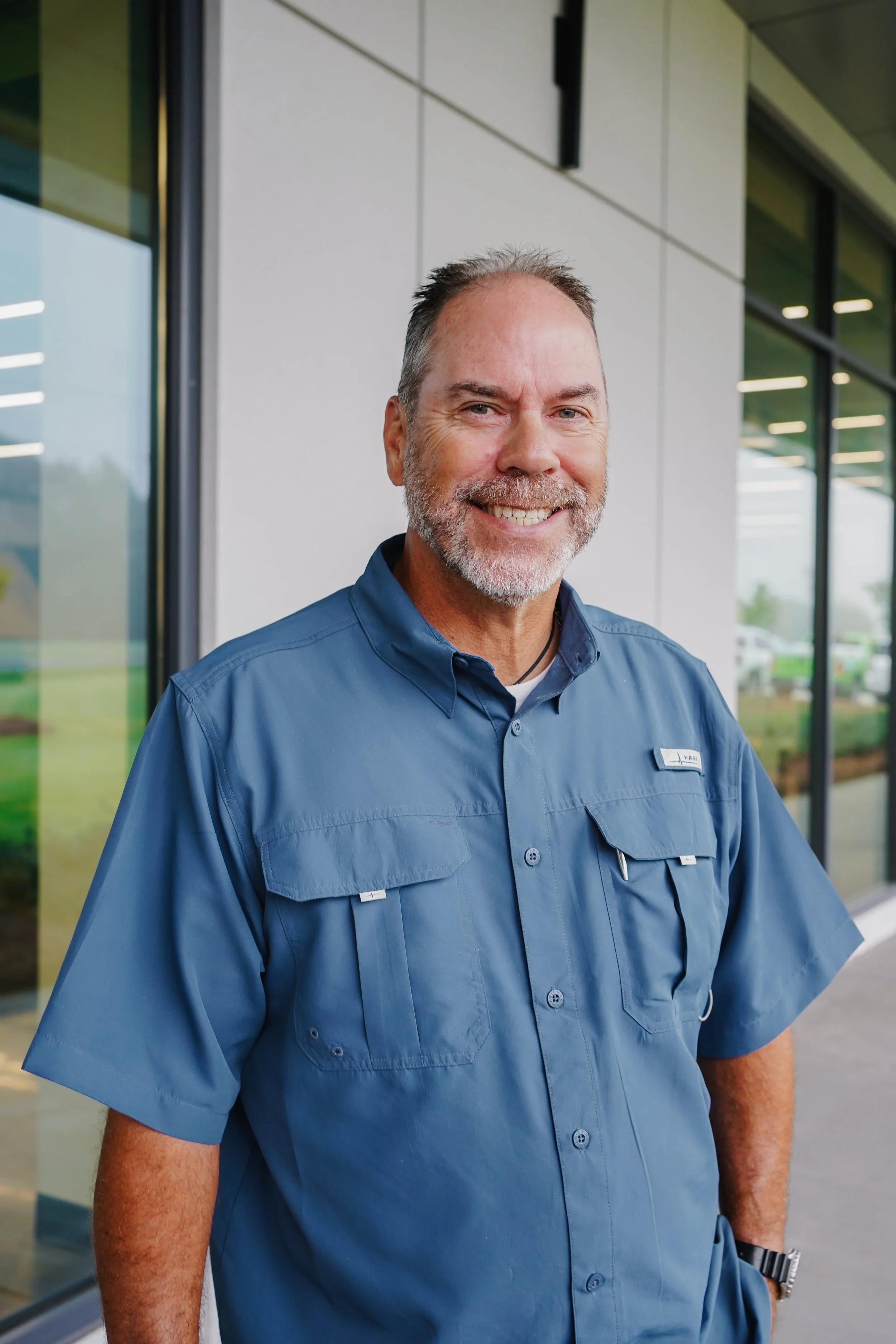 A smiling man in a blue uniform standing outside a modern building.