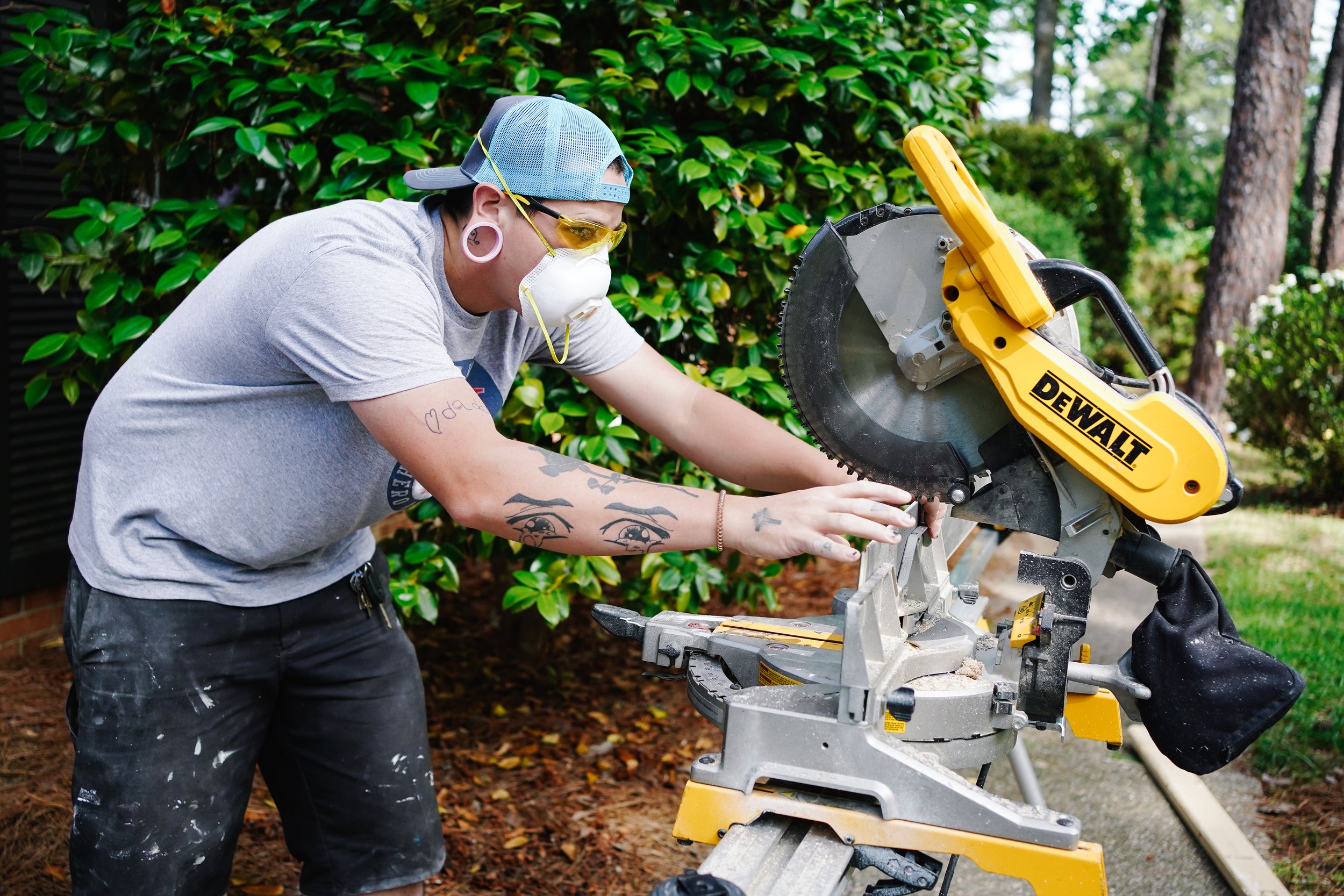 Person using a yellow DEWALT miter saw outdoors with greenery in background.