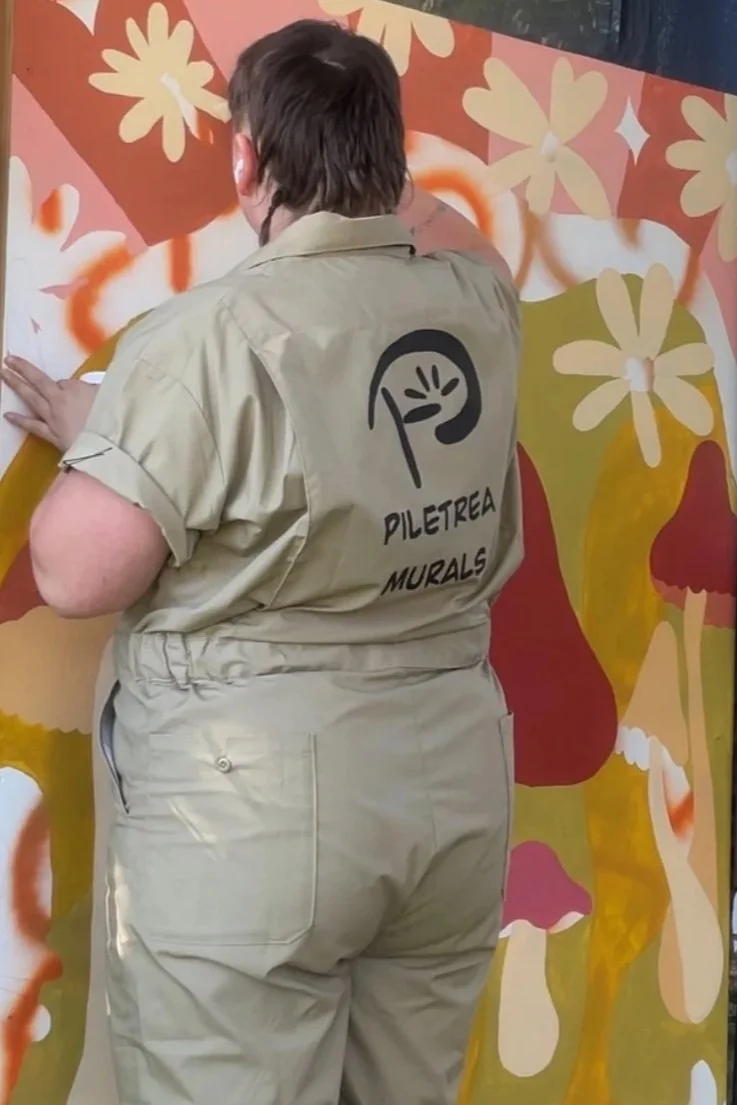 Person working on a mural at Piletrea Murals, painting floral designs on a wall.
