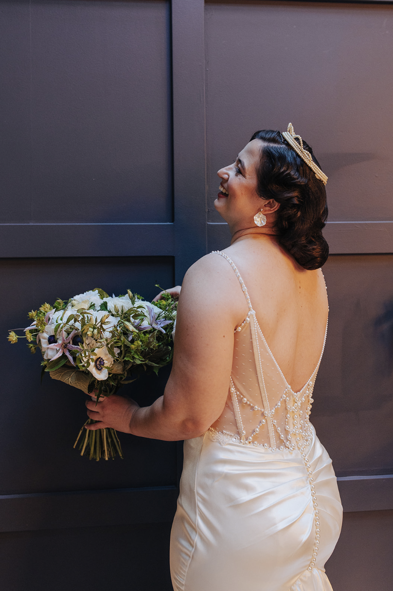 A woman in a wedding dress holding a bouquet of flowers, smiling and looking to her left.