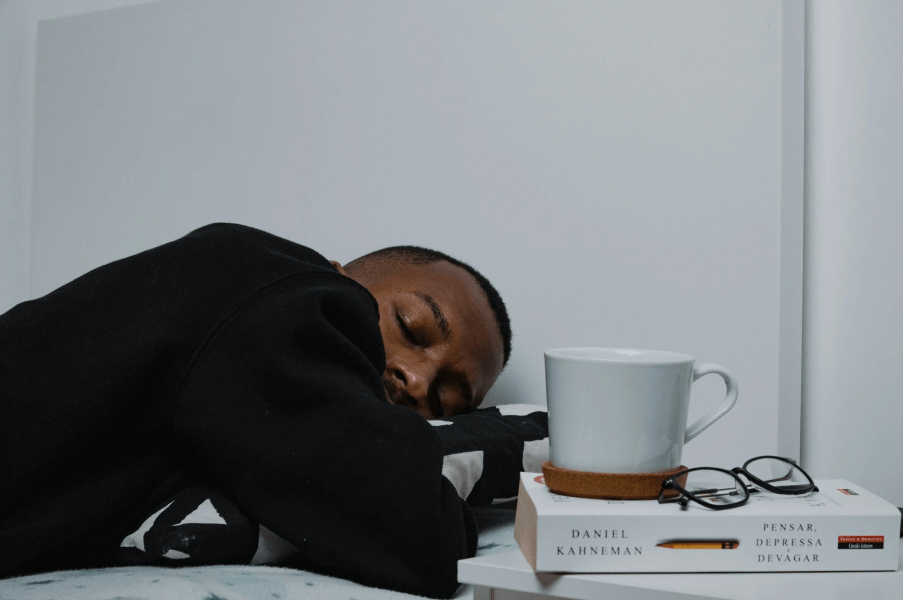 A young man with excellent eyebrow grooming habits and a fresh line-up has fallen asleep after placing his glasses on a small table beside a tea mug.
