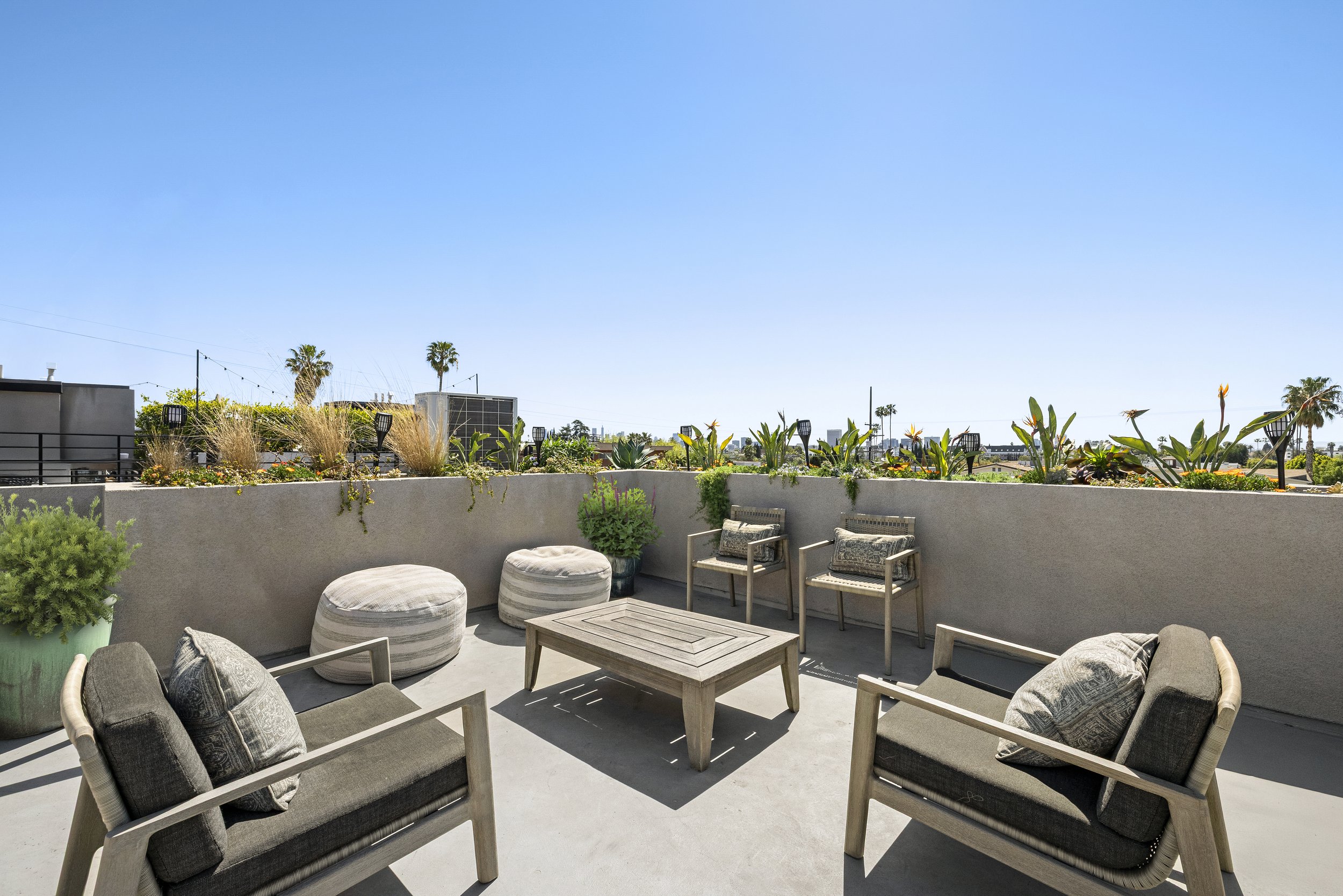 Outdoor rooftop patio with seating area, plants, and clear blue sky.