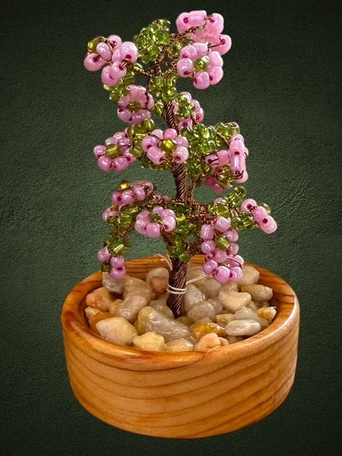 Bead and wire miniature tree with pink and green beads in a wooden pot filled with small stones.