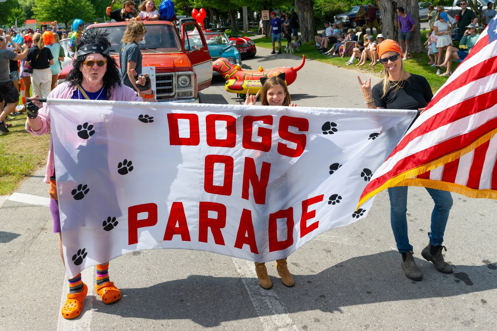 People participating in a parade holding a banner that reads 'Dogs on Parade' with paw prints, surrounded by a crowd of spectators and floats in the background.