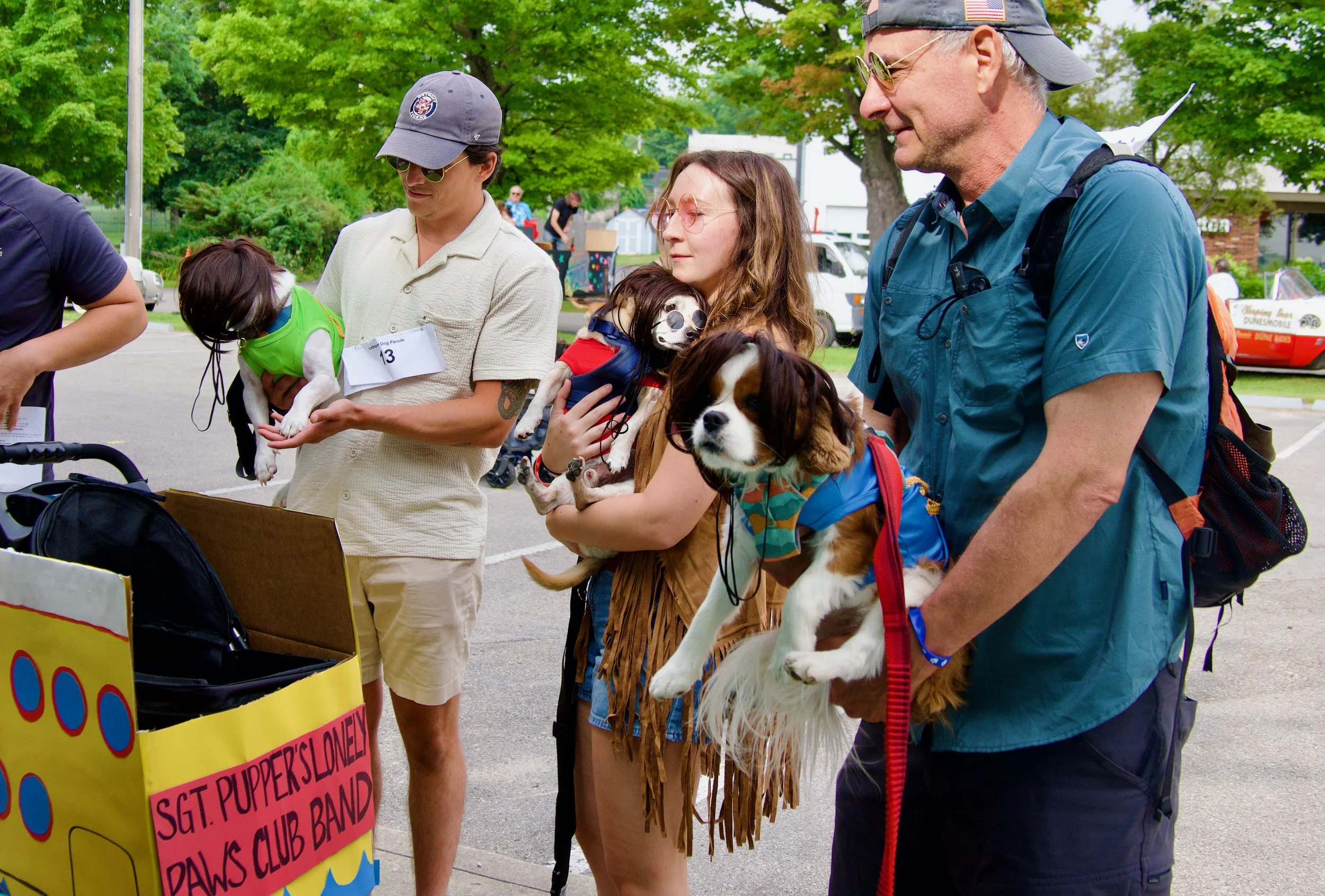 People holding dogs at an outdoor event with trees and tents in the background.