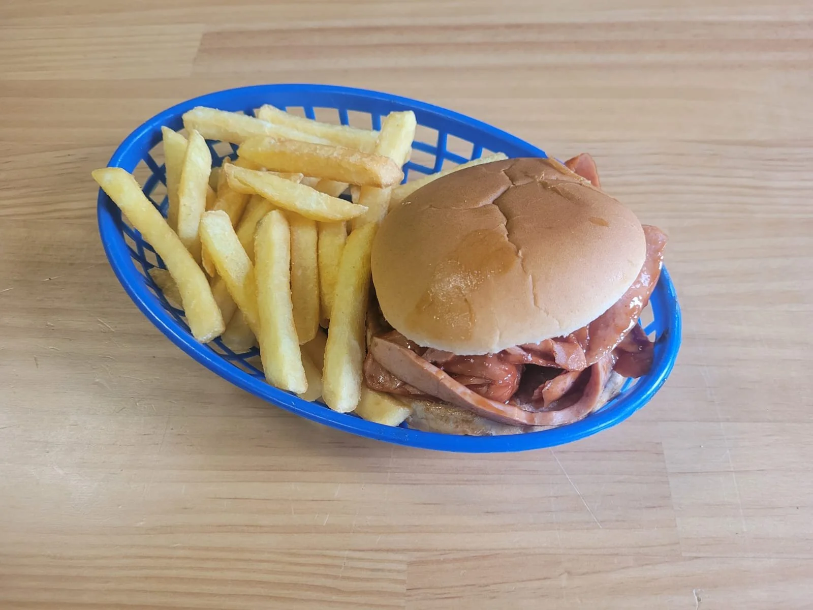 French fries and a sandwich with meat and sauce in a blue basket on a wooden table.