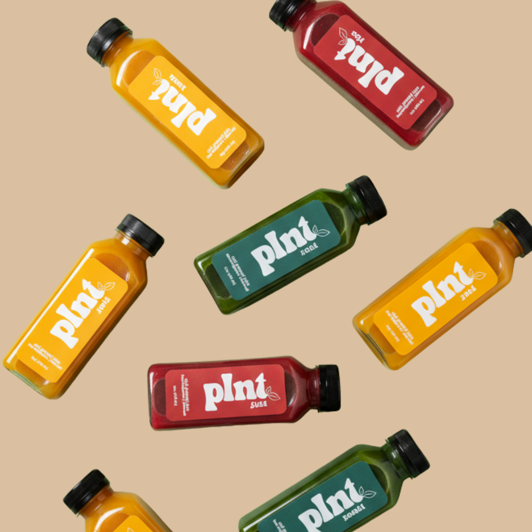 Multiple bottles of green, yellow, and red plant-based juice on a beige background.