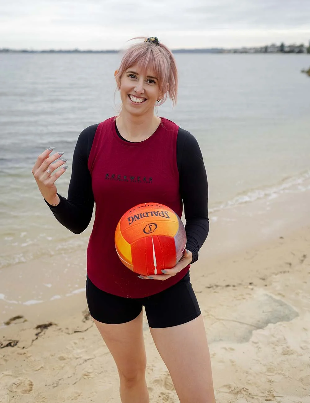 Amber McGhie smiling black and red sports outfit holding a volleyball at Cottesloe. Financial adviser by trade, plays indoor beach volleyball in the super league in her spare time.