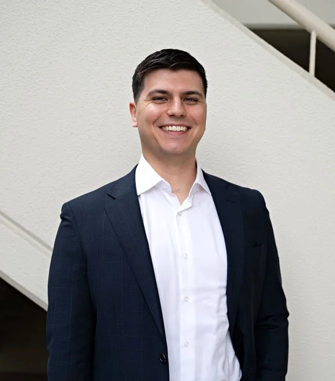 Financial Adviser Adrian smiling at the camera in a crisp navy suit and open collar white shirt