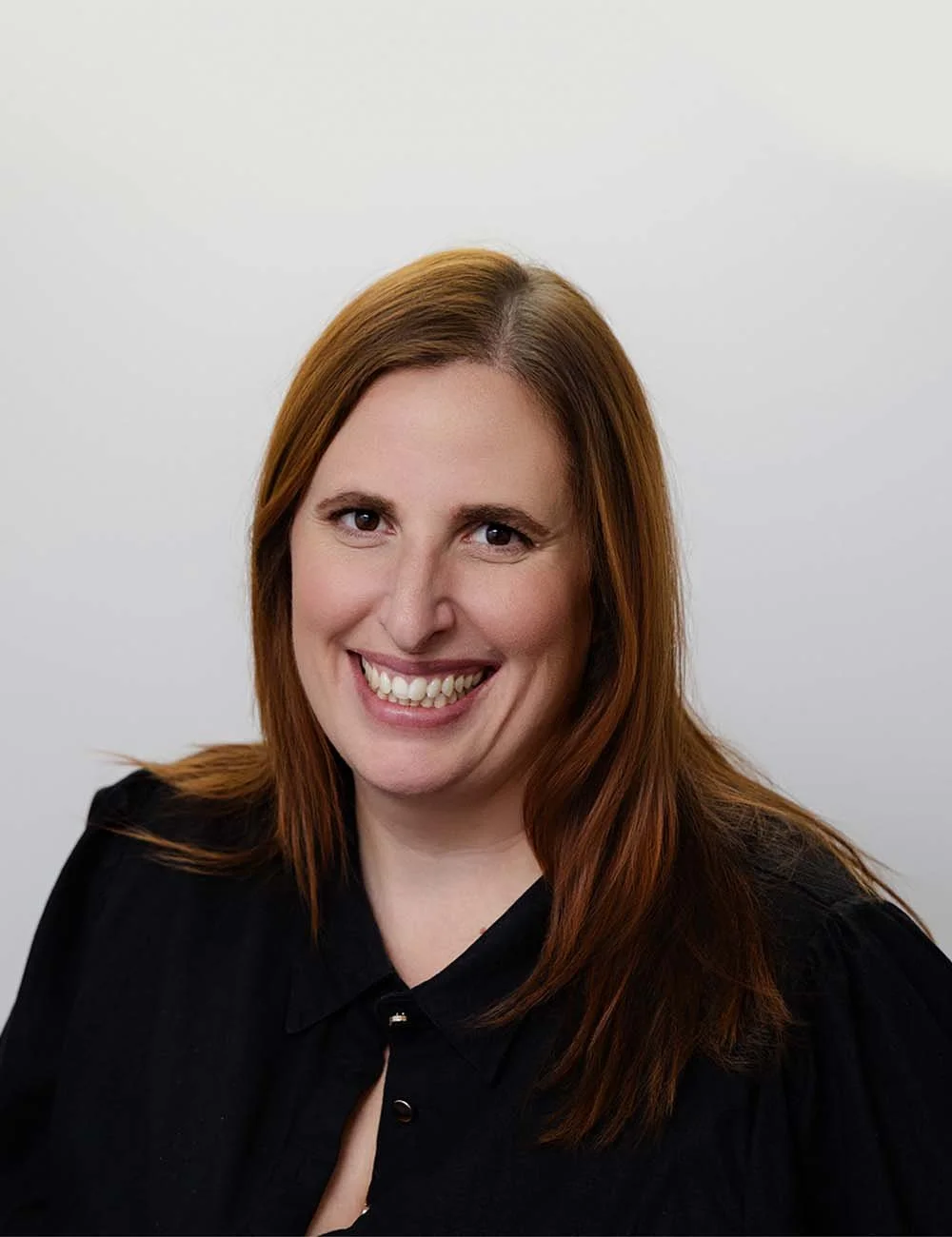 Close-up of Nicole Andrews, practice manager at a financial advice firm in Perth. with shoulder-length red hair, smiling, against a plain white background, wearing a black top.