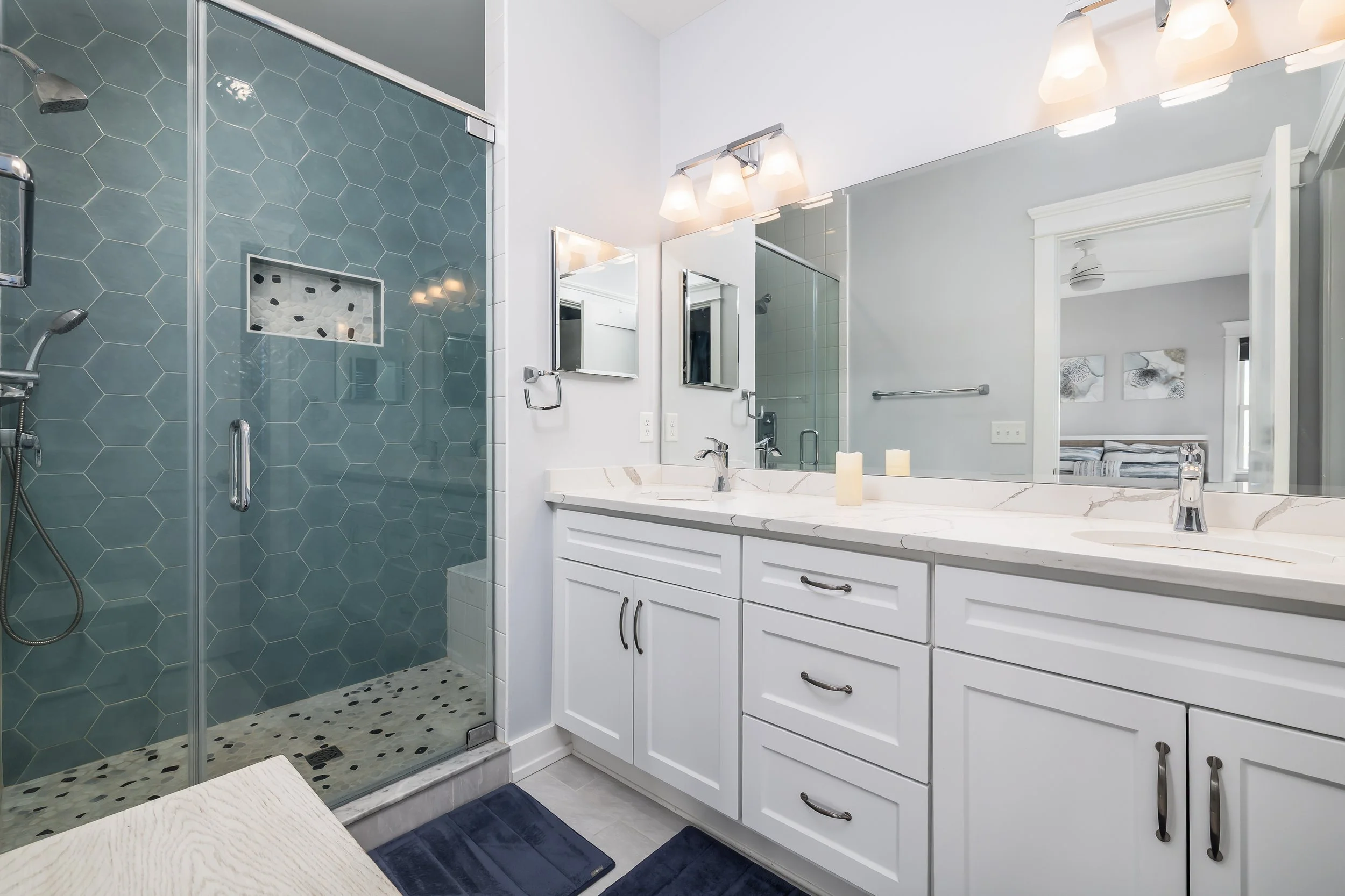 A modern bathroom with a white double vanity, large mirror, and green hexagon tile shower area.
