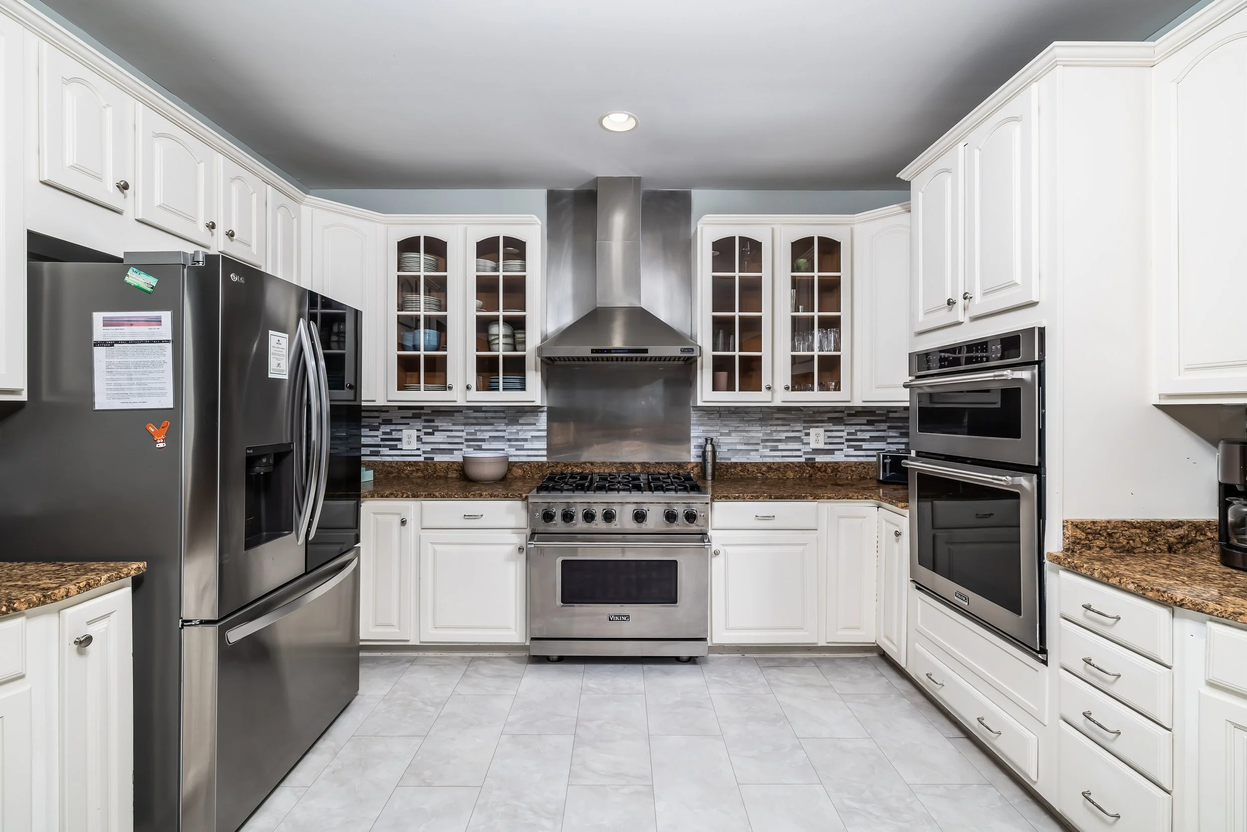 Modern kitchen with white cabinets, stainless steel appliances, brown granite countertops, and gray tile backsplash.