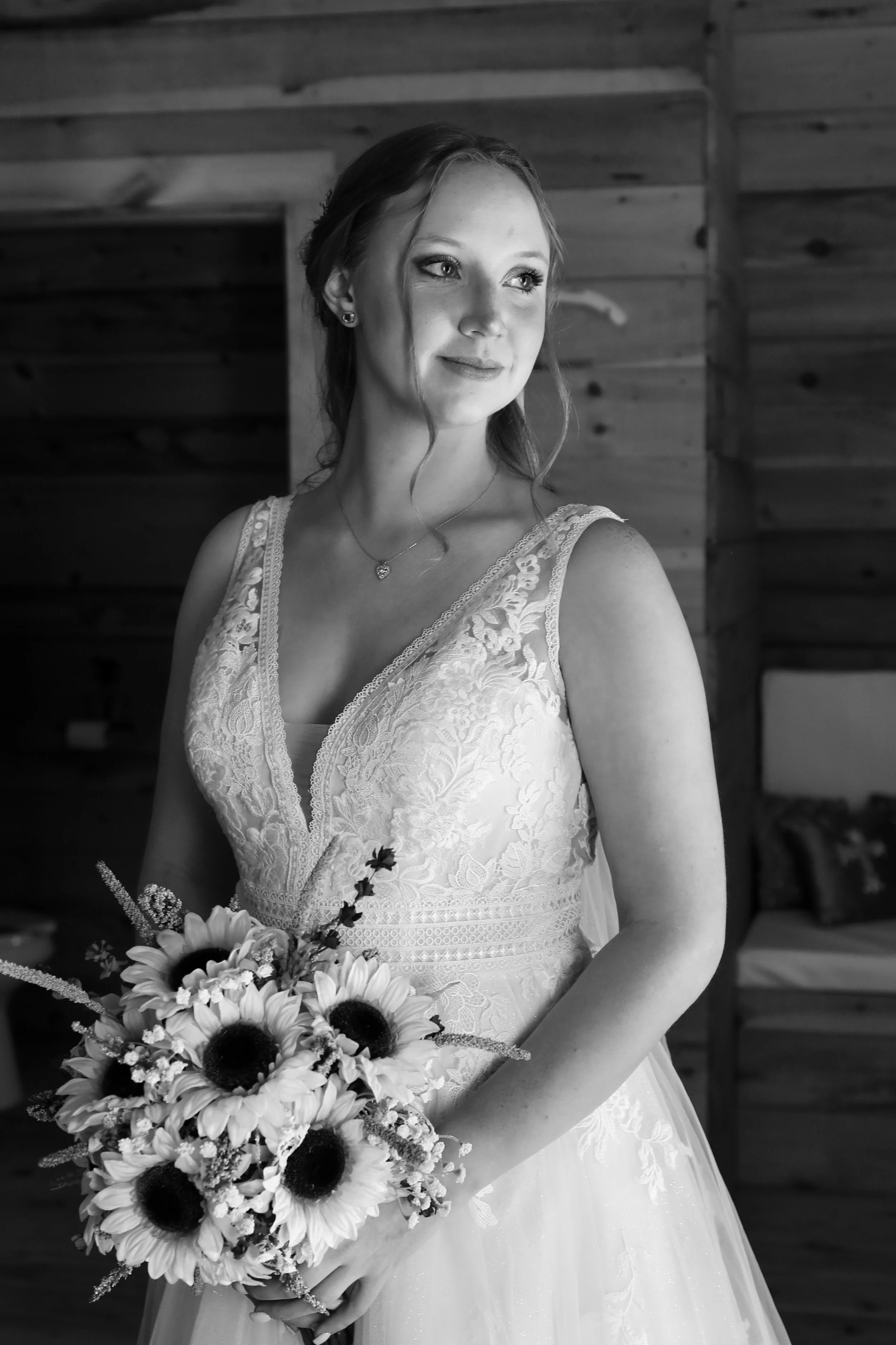 A young woman in a wedding dress holding a bouquet of flowers, standing indoors with wood-paneled walls in the background.