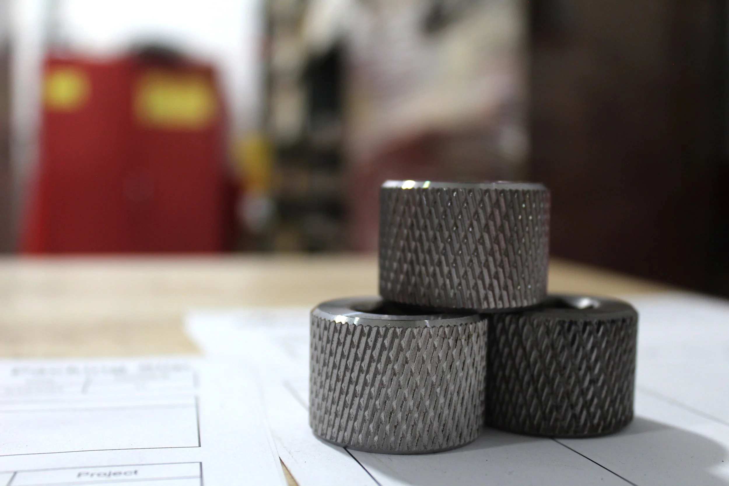 Three metallic cylindrical objects stacked on top of each other on a piece of paper with printed boxes and lines, with a blurred background.