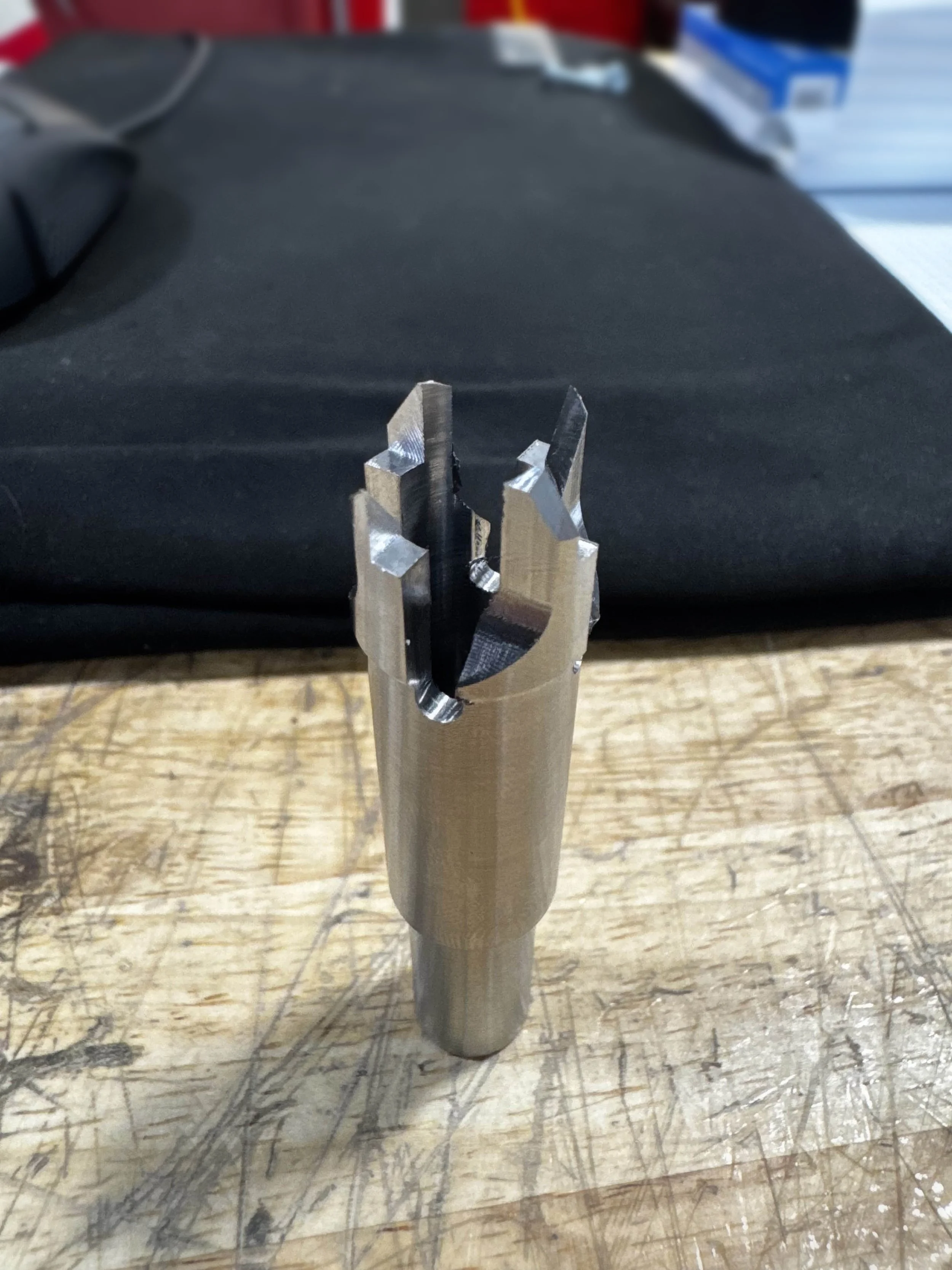 A metal CNC-machined tool holder with a tapered shank and a jaw-like cutting interface, placed on a wooden workbench.