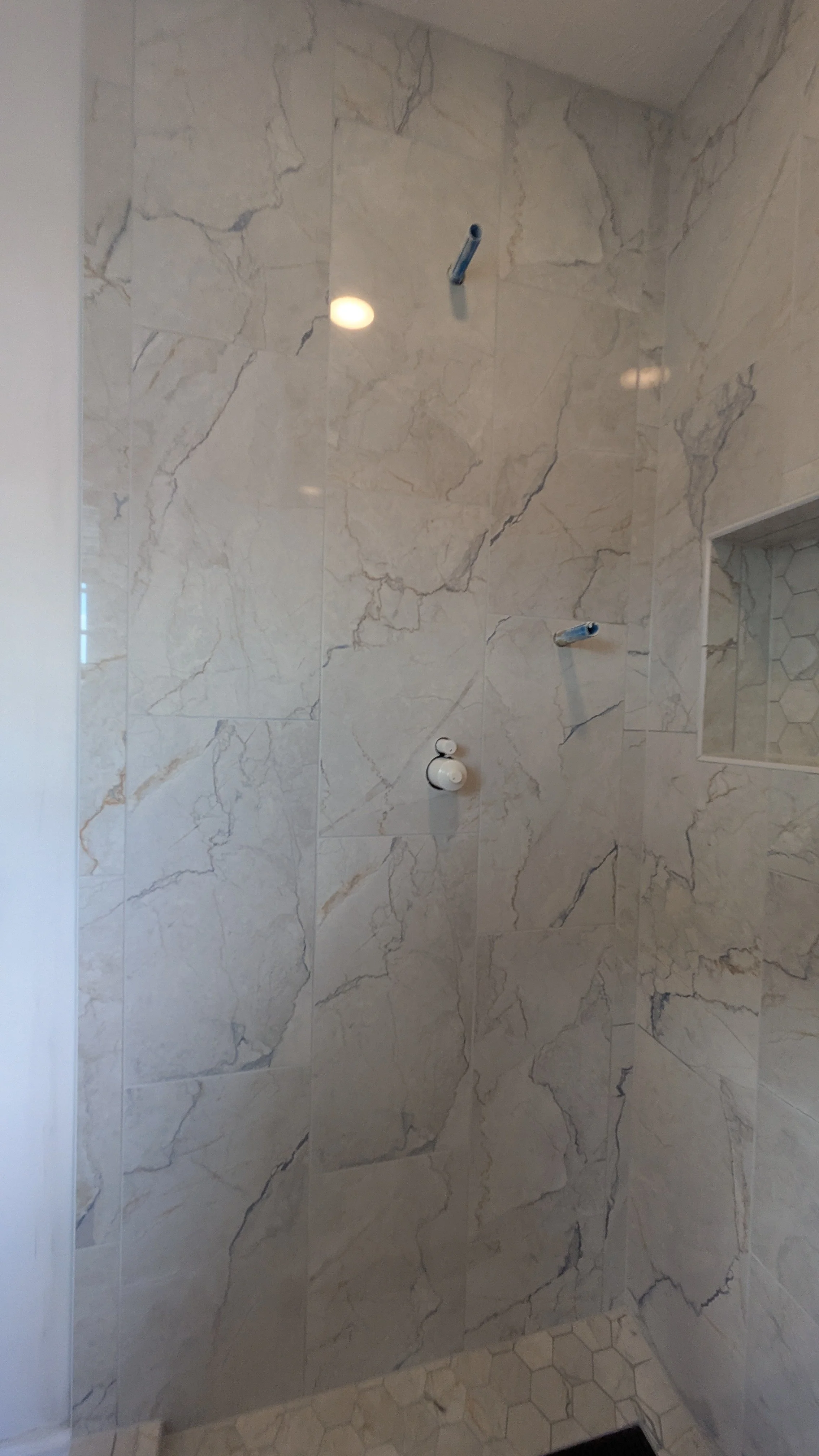 Empty shower with marble tile walls and hexagonal tile floor, no fixtures installed yet.