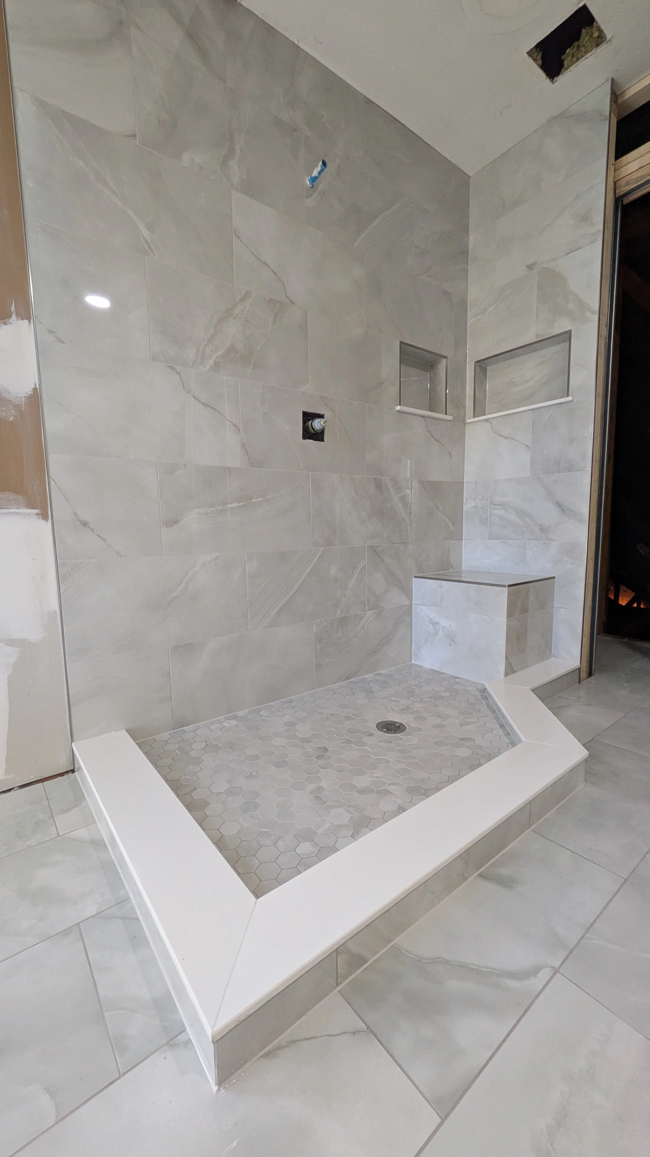 Bathroom shower with gray marble tiles, built-in niches, and a hexagonal tile shower floor.